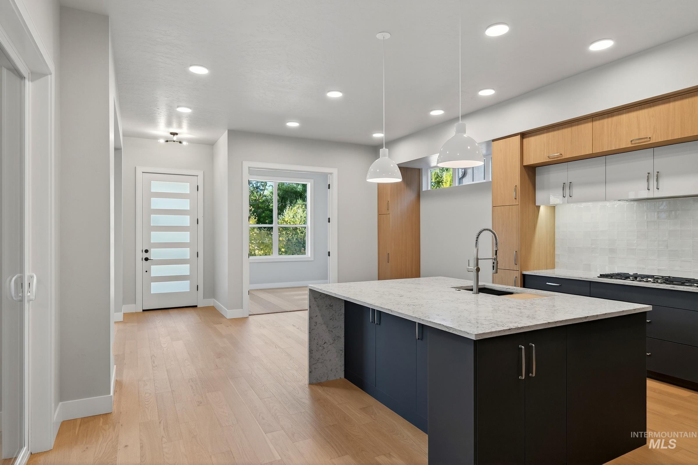 Kitchen with decorative backsplash, light stone counters, pendant lighting, light wood-type flooring, and a kitchen island with sink