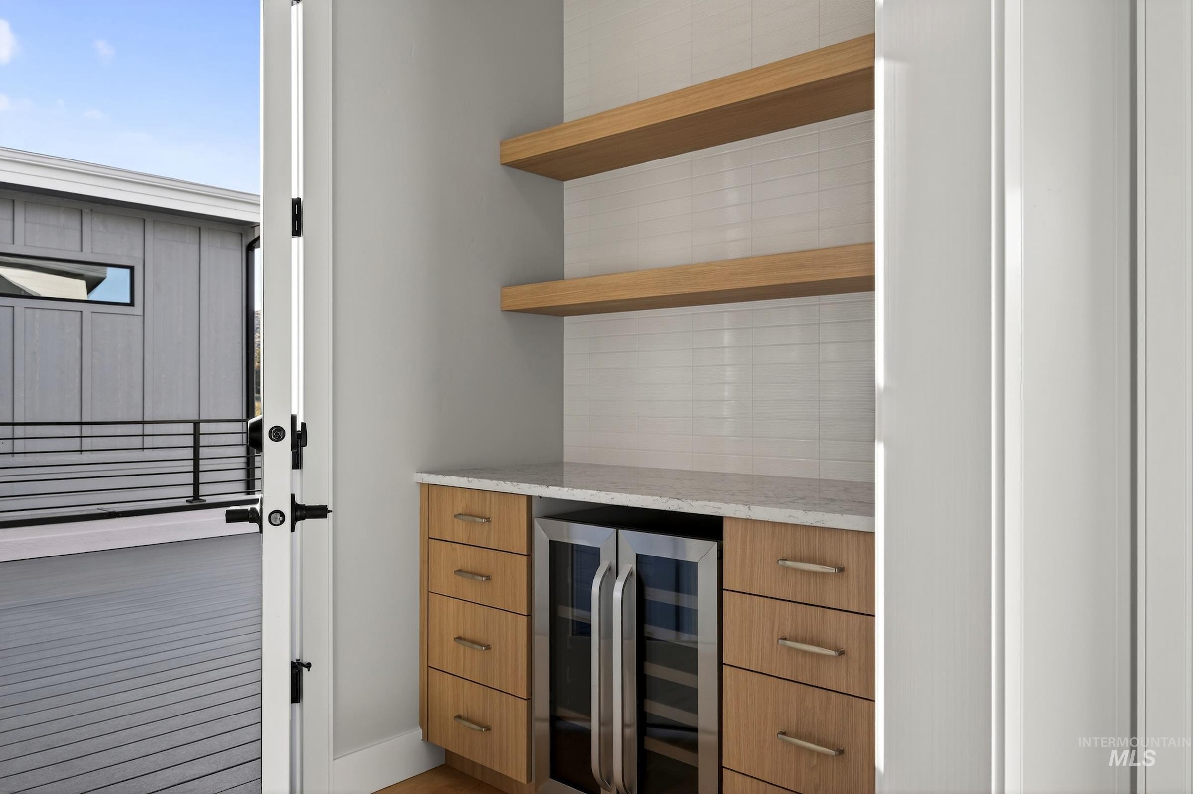 Bar with light stone counters, beverage cooler, open shelves, modern cabinets, and decorative backsplash