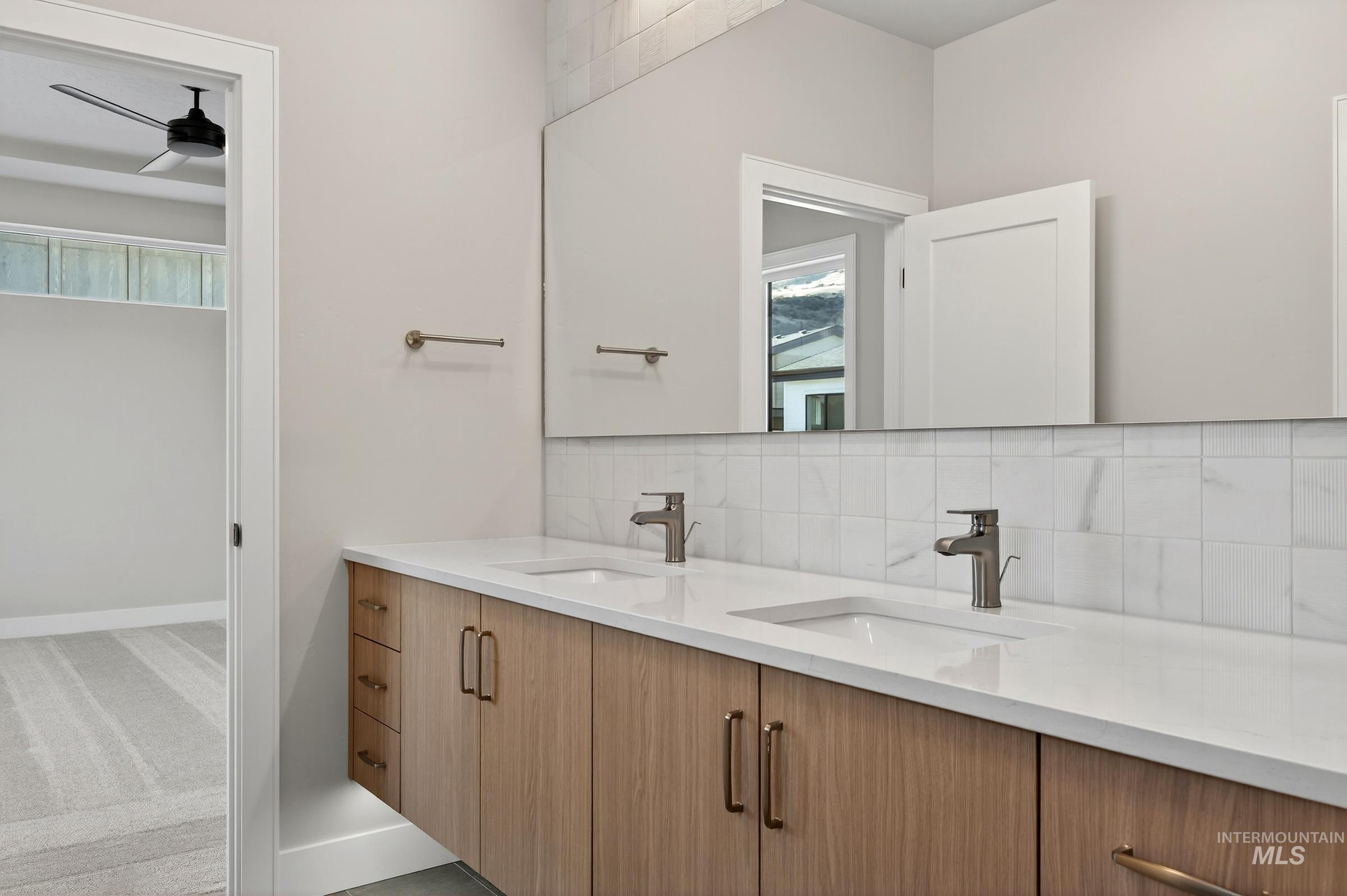 Bathroom featuring backsplash, double vanity, ceiling fan, and light colored carpet