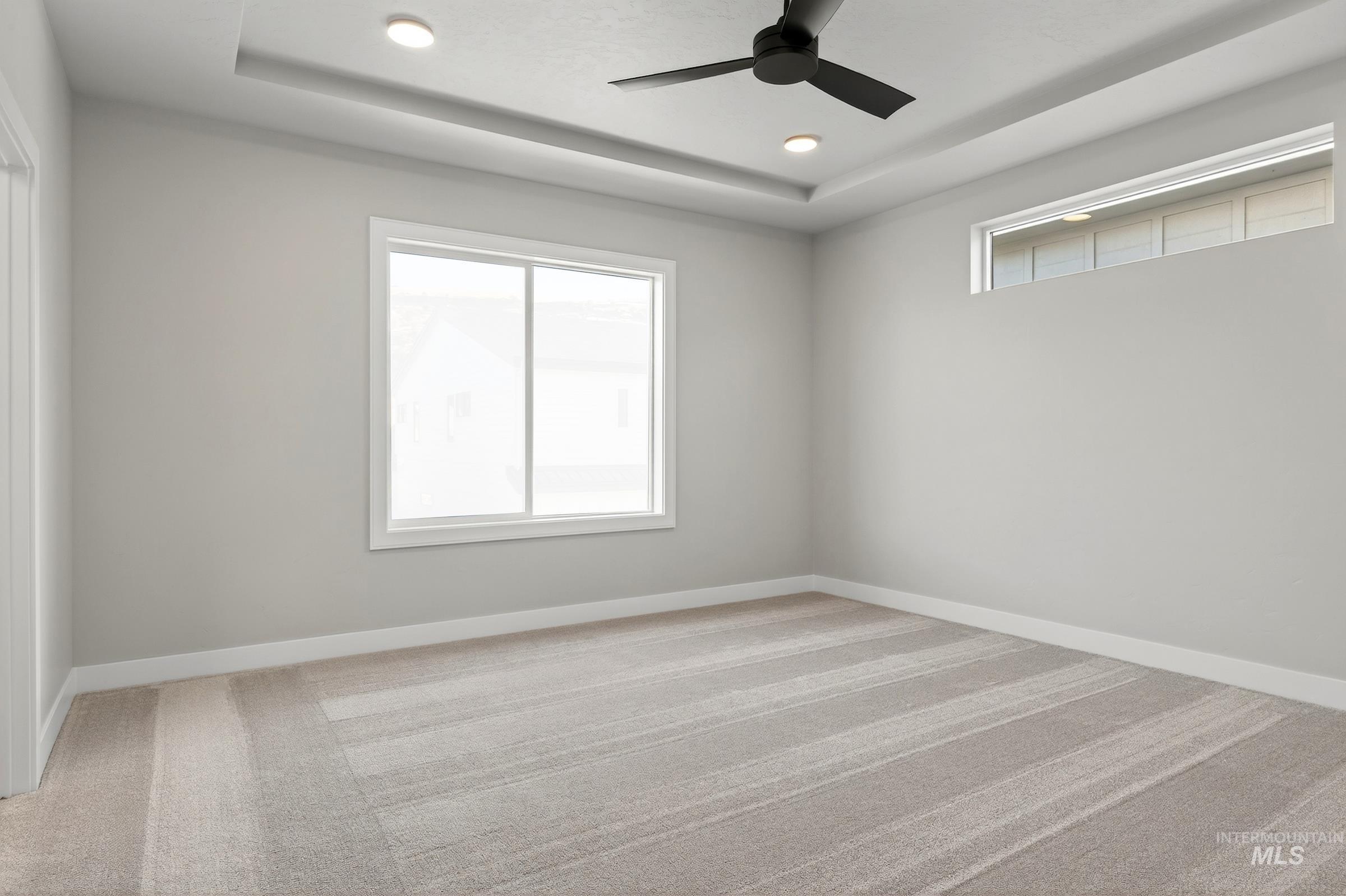 Empty room with a tray ceiling, light colored carpet, recessed lighting, and a ceiling fan