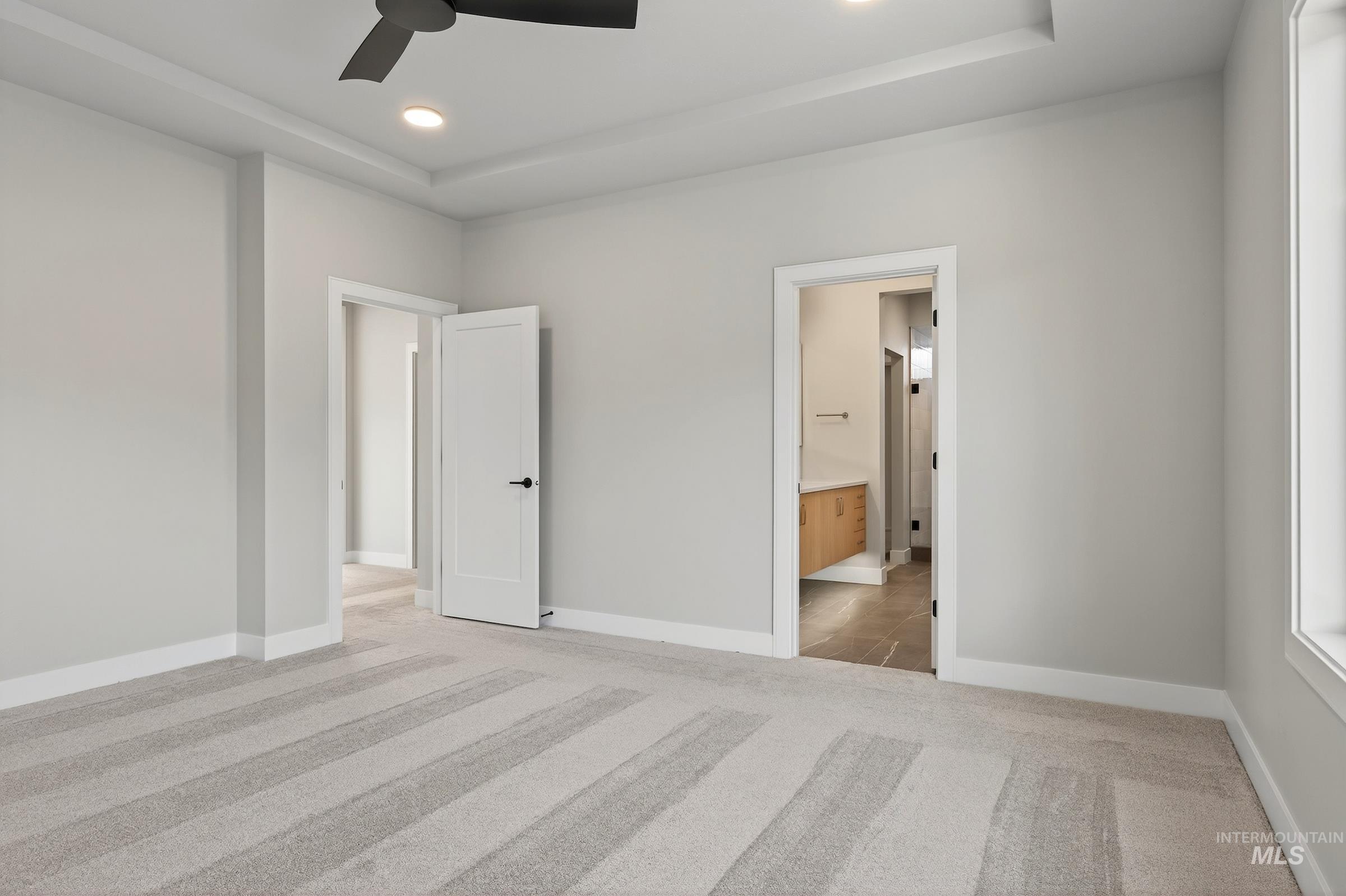 Unfurnished bedroom featuring light carpet, ceiling fan, recessed lighting, a raised ceiling, and connected bathroom