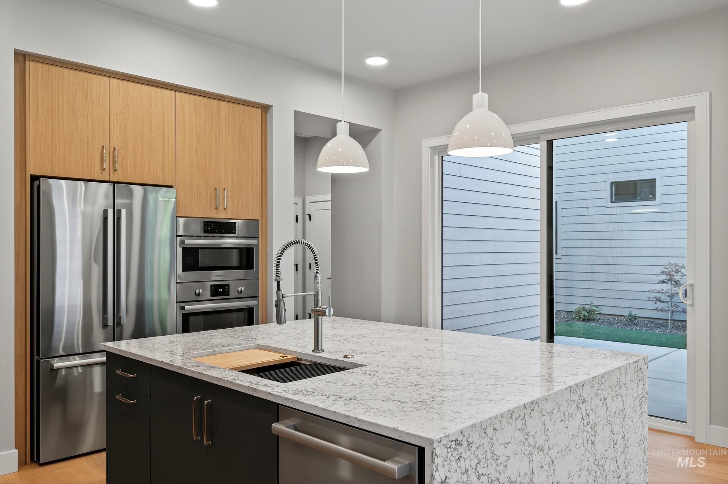 Kitchen with light wood-type flooring, appliances with stainless steel finishes, decorative light fixtures, light stone counters, and recessed lighting