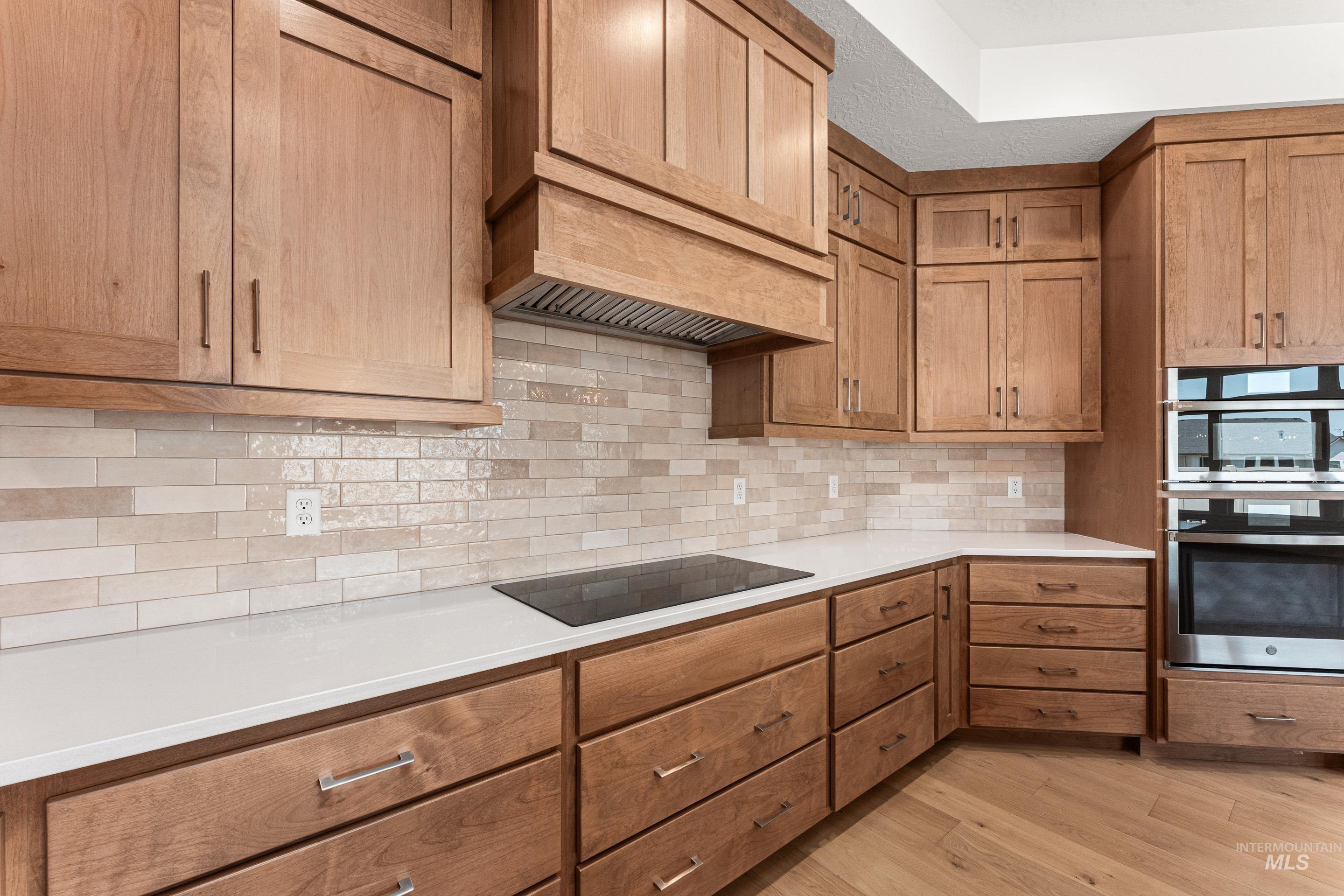 Kitchen featuring tasteful backsplash, light wood finished floors, black electric cooktop, brown cabinets, and light stone counters