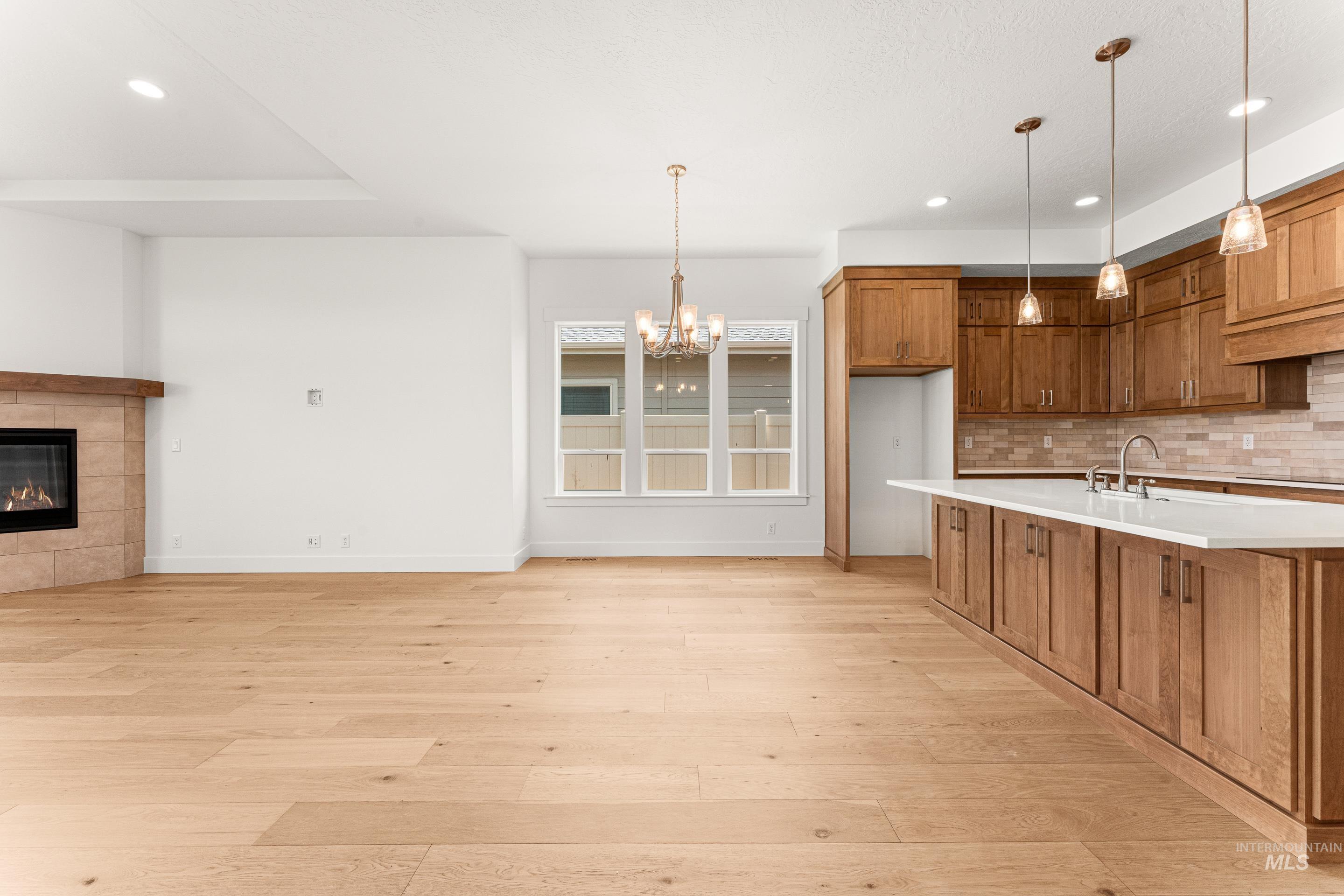 Kitchen featuring brown cabinetry, recessed lighting, hanging light fixtures, tasteful backsplash, and a tile fireplace