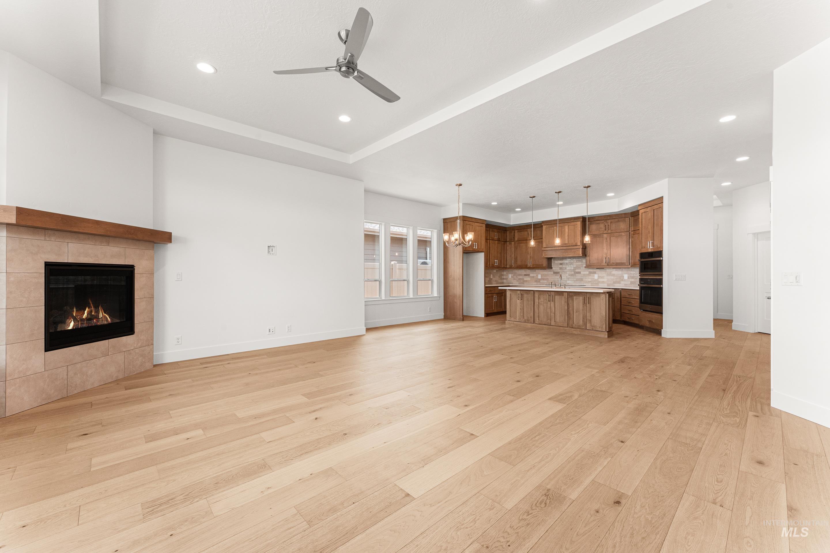Unfurnished living room with a chandelier, recessed lighting, a ceiling fan, light wood-style floors, and a tray ceiling