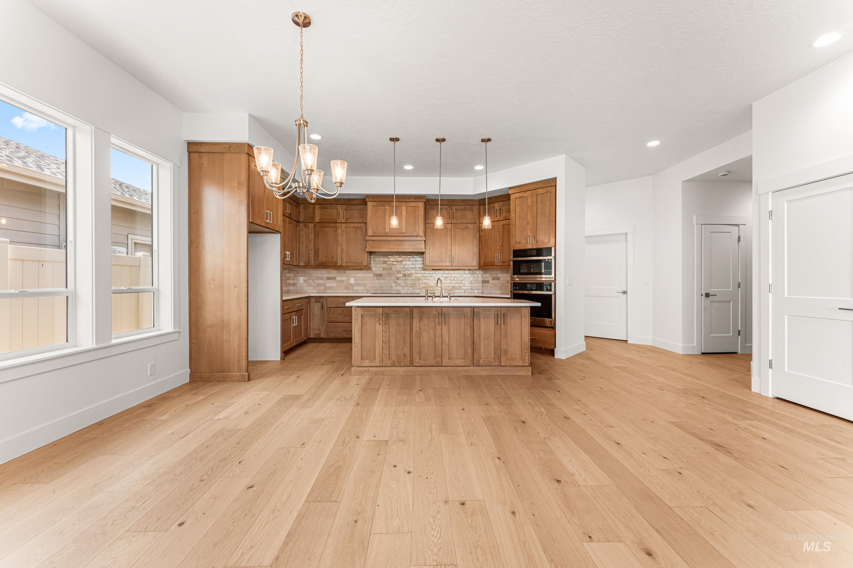 Kitchen featuring brown cabinetry, light countertops, hanging light fixtures, a kitchen island with sink, and a chandelier