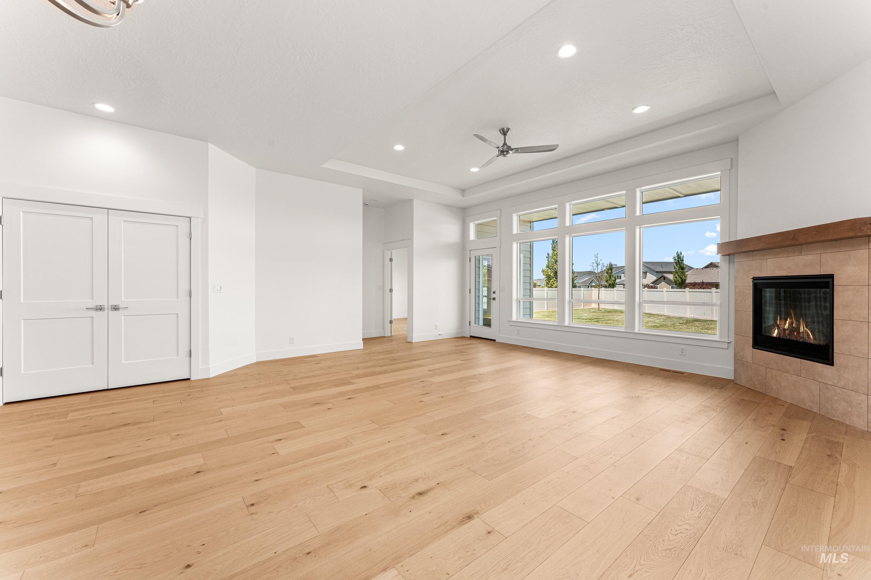 Unfurnished living room featuring a tray ceiling, light wood-type flooring, a fireplace, recessed lighting, and a ceiling fan