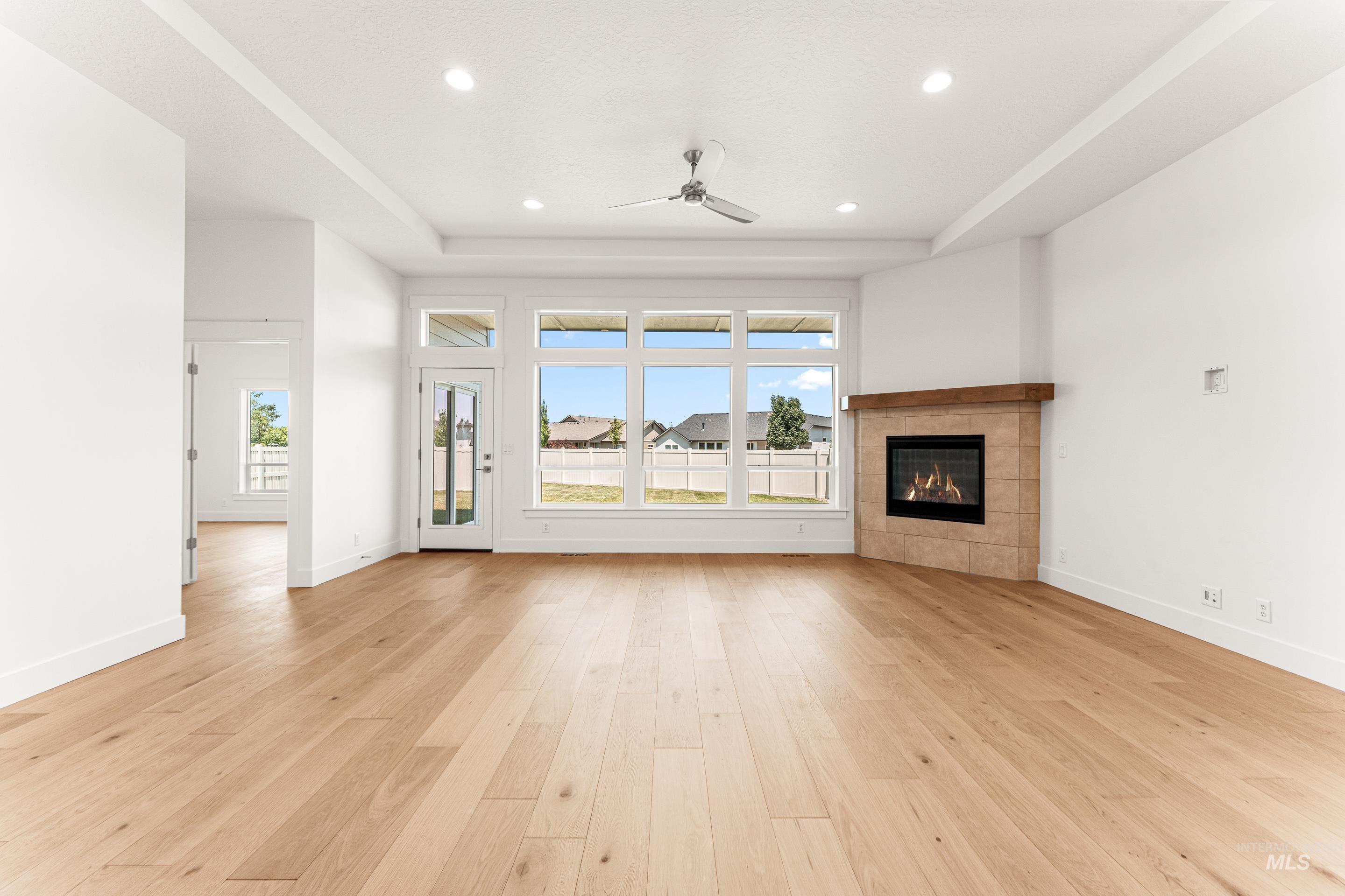 Unfurnished living room with a tile fireplace, a ceiling fan, light wood-style flooring, a raised ceiling, and recessed lighting