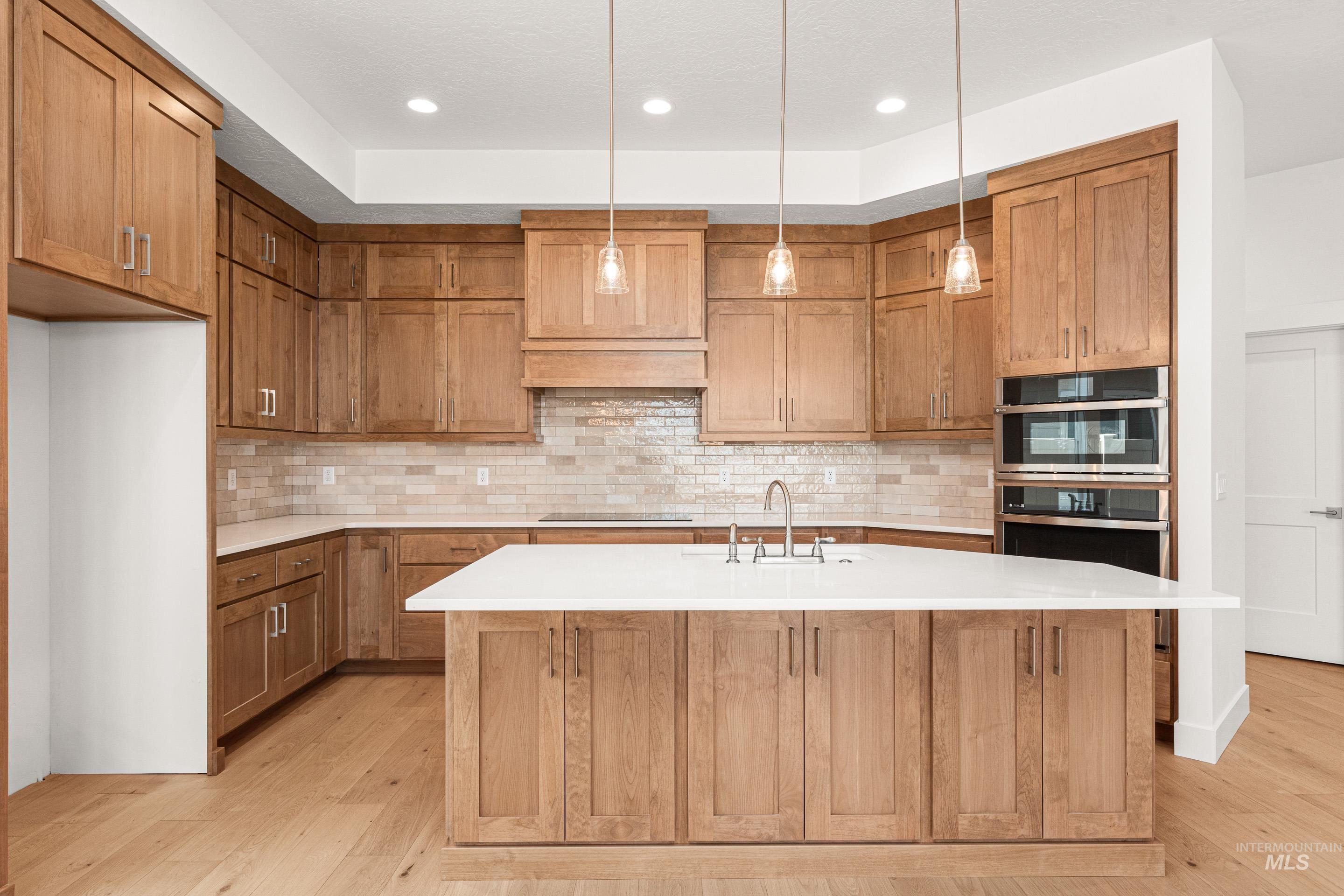 Kitchen featuring brown cabinets, light wood finished floors, recessed lighting, hanging light fixtures, and backsplash
