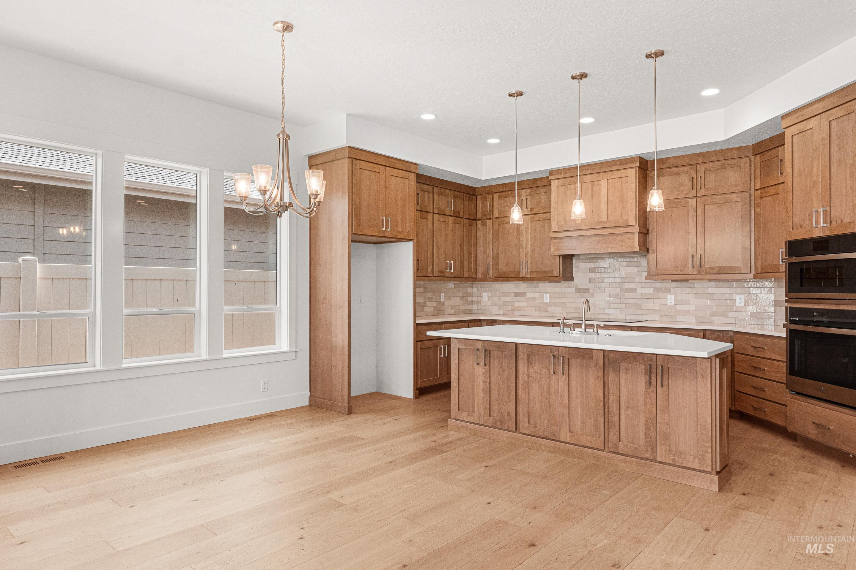 Kitchen featuring brown cabinetry, tasteful backsplash, decorative light fixtures, a chandelier, and recessed lighting