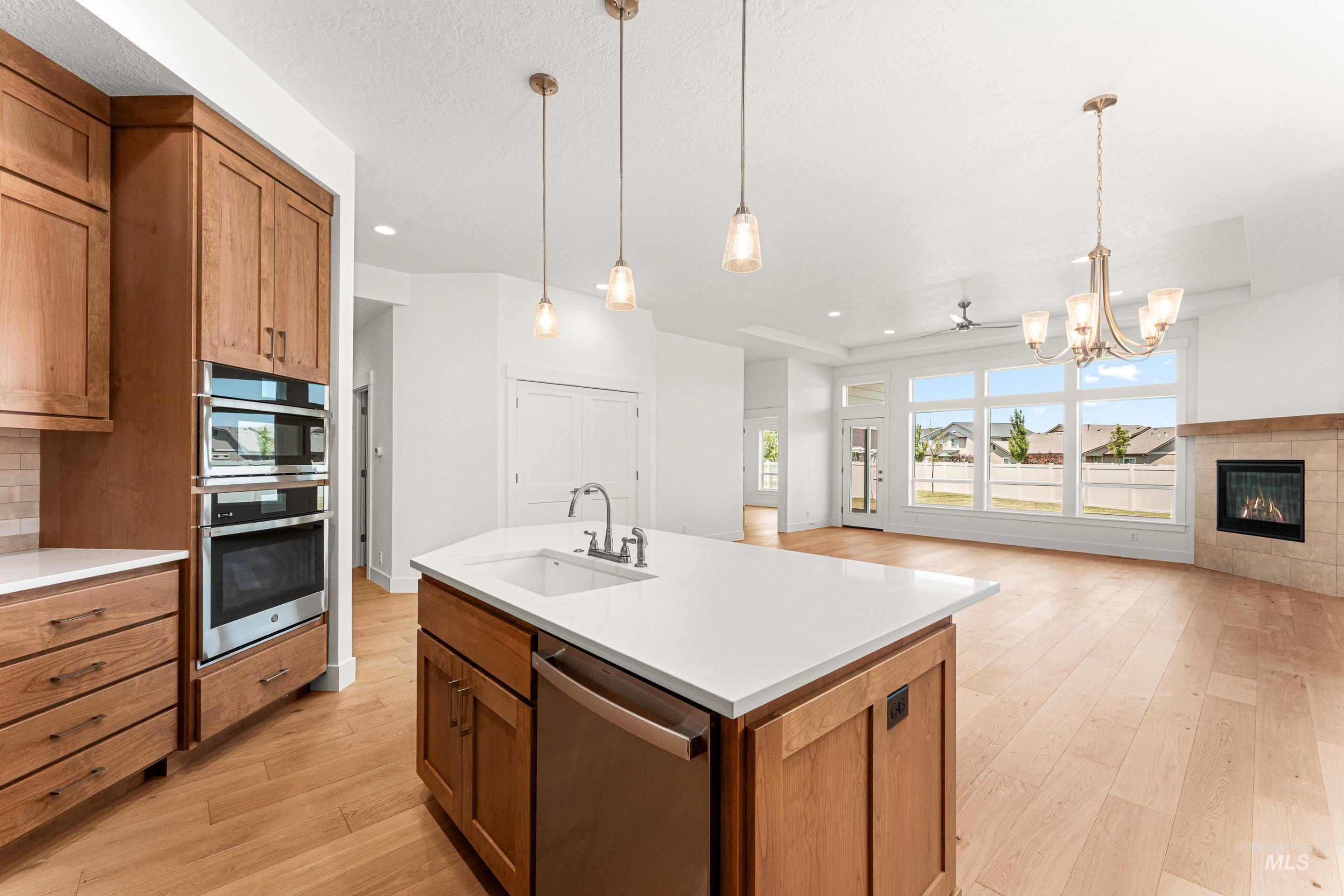 Kitchen with brown cabinets, appliances with stainless steel finishes, light wood-type flooring, decorative light fixtures, and open floor plan