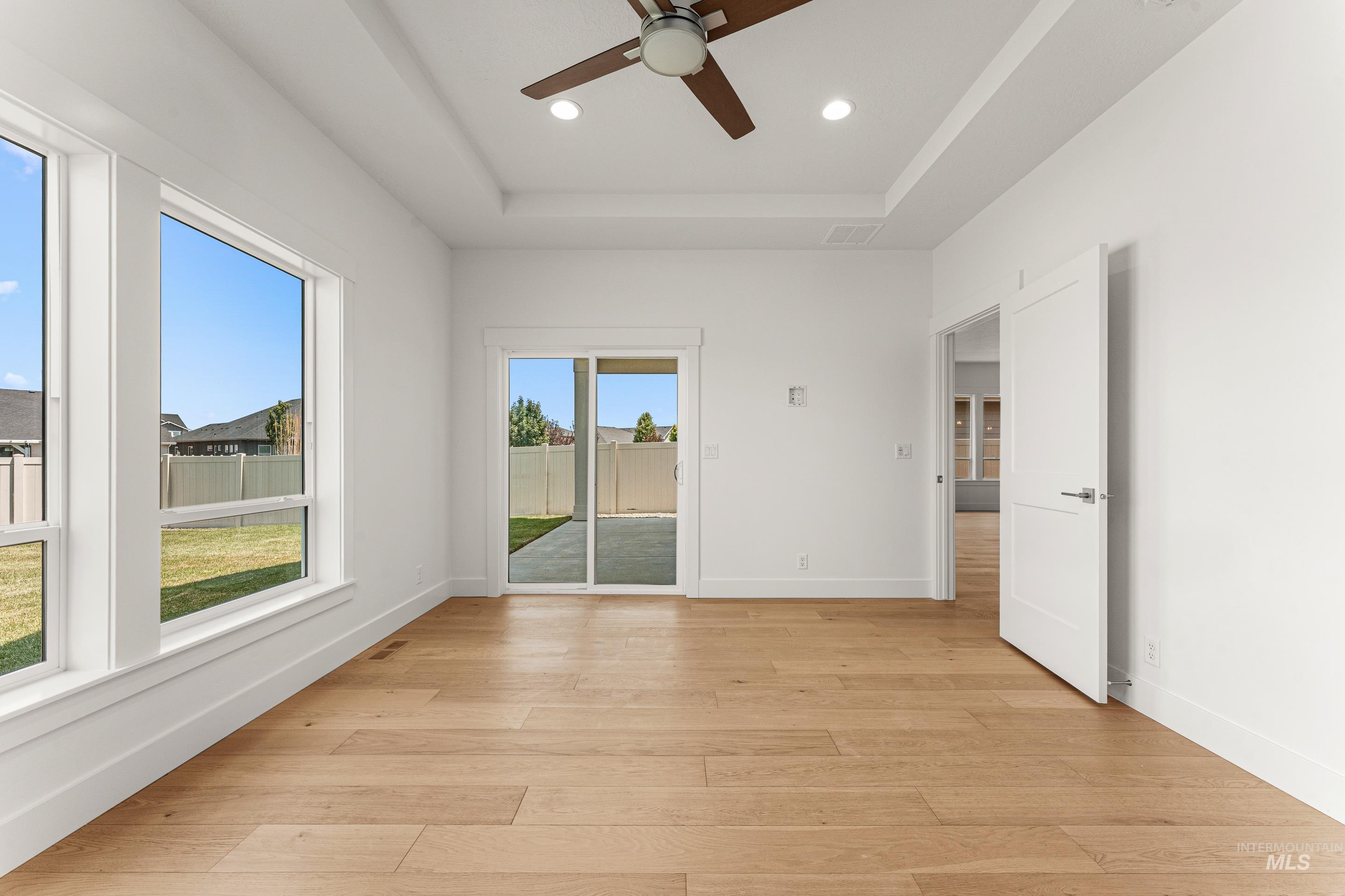 Empty room featuring a raised ceiling, light wood-style floors, recessed lighting, and ceiling fan