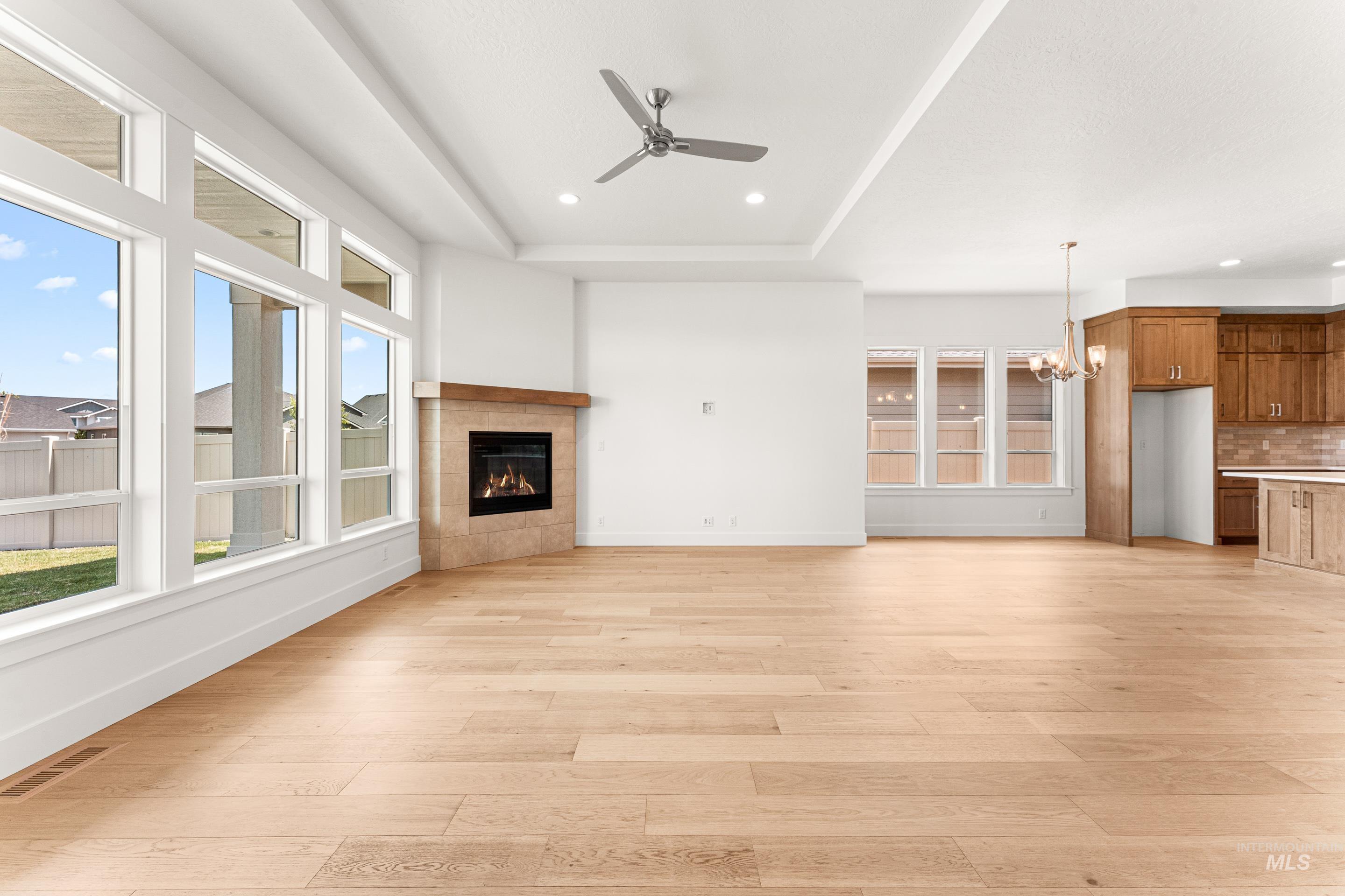 Unfurnished living room featuring light wood-type flooring, a tile fireplace, a raised ceiling, a chandelier, and recessed lighting