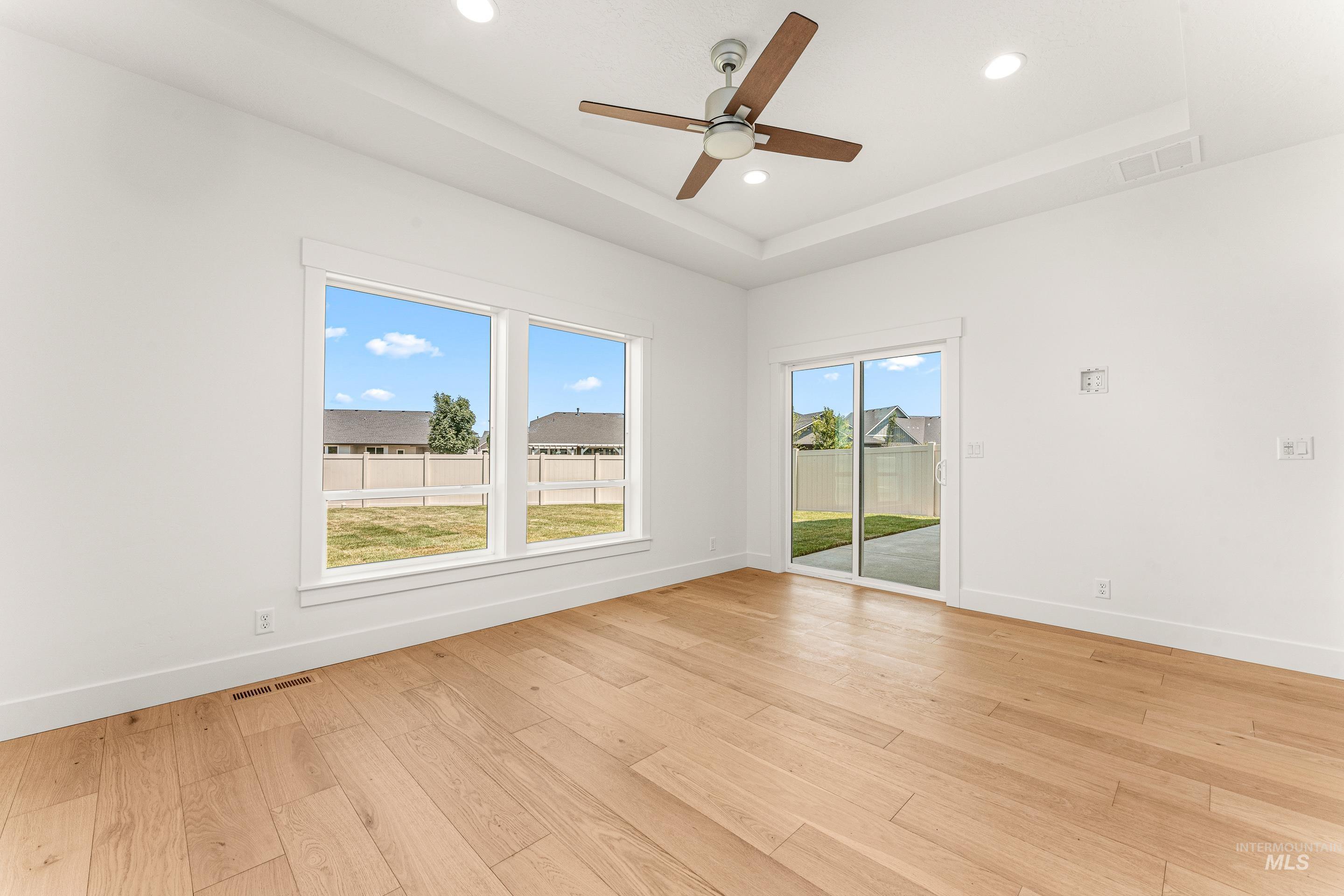Spare room with a tray ceiling, healthy amount of natural light, light wood-style flooring, ceiling fan, and recessed lighting