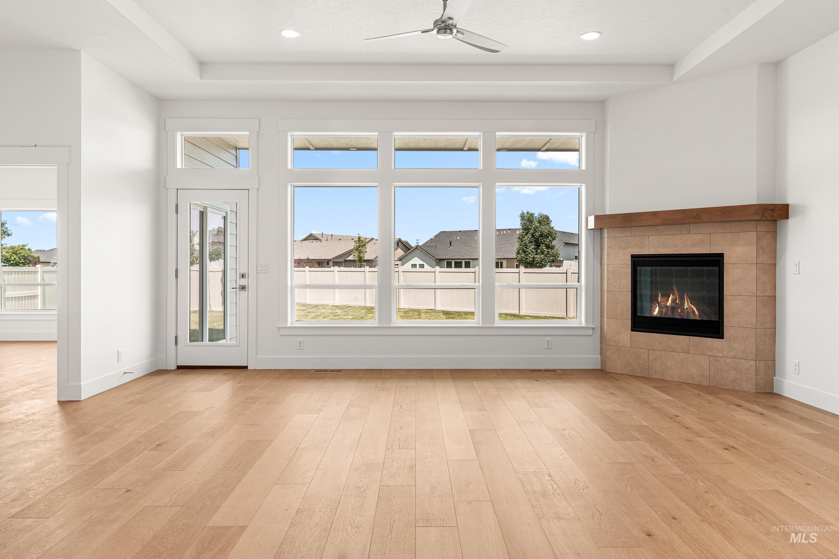 Unfurnished living room featuring light wood-style flooring, a tile fireplace, recessed lighting, a raised ceiling, and ceiling fan