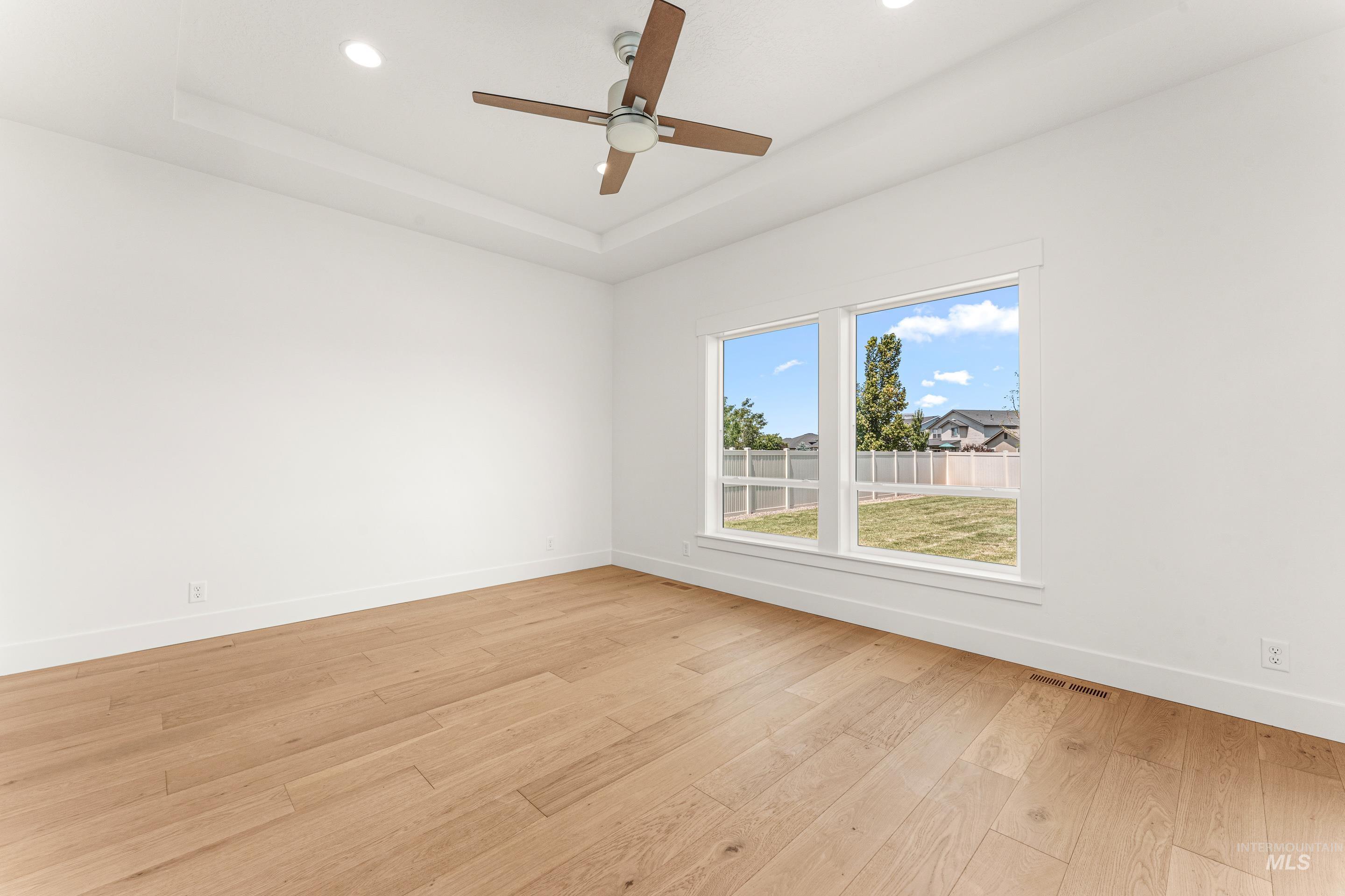 Empty room featuring a tray ceiling, light wood-style floors, recessed lighting, and a ceiling fan