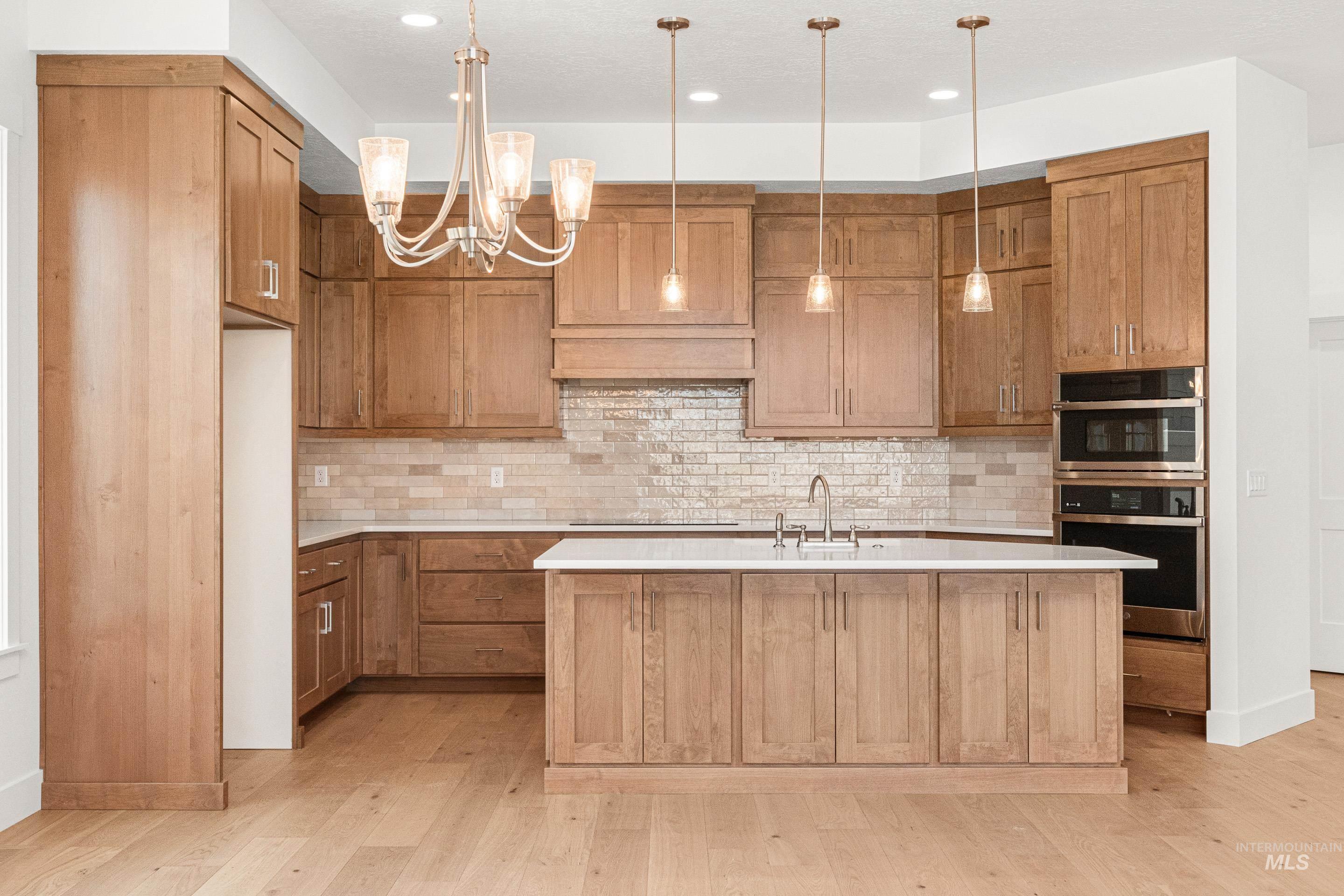 Kitchen with brown cabinetry, a center island with sink, backsplash, a chandelier, and recessed lighting