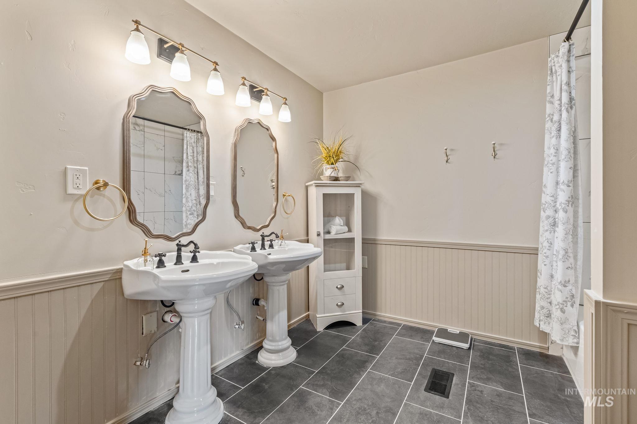 Bathroom featuring dual pedestal sinks with black fixtures, framed mirrors, and wall-mounted light fixtures