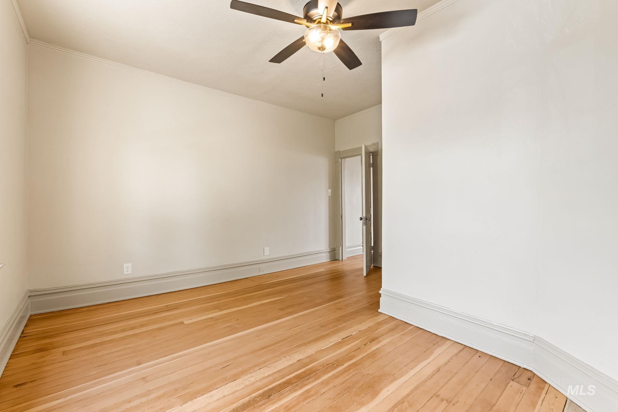 Room featuring wood-finish flooring, light-toned walls, a ceiling fan with integrated lighting, and crown molding