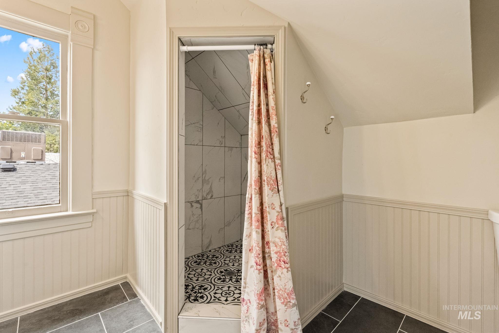 Tiled shower with decorative floor, white marble-look wall tiling, and sloped ceiling