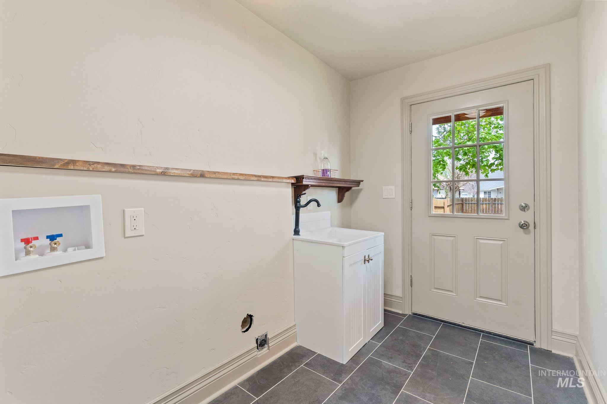 Utility room with dark tile flooring, a white paneled door with windowpanes, and a utility sink with a black faucet