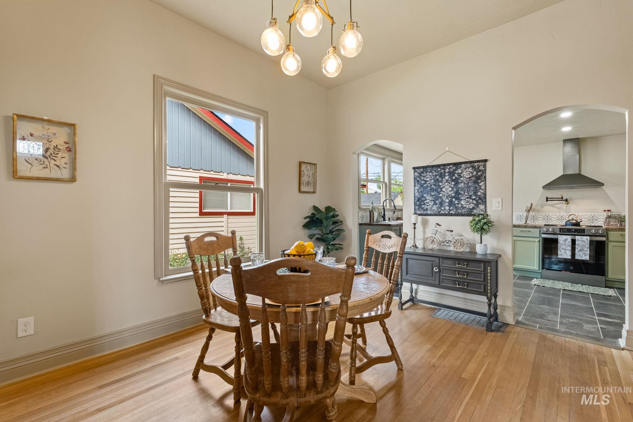 Bright dining space featuring wood-finish flooring, a contemporary chandelier, and an arched doorway opening to the kitchen