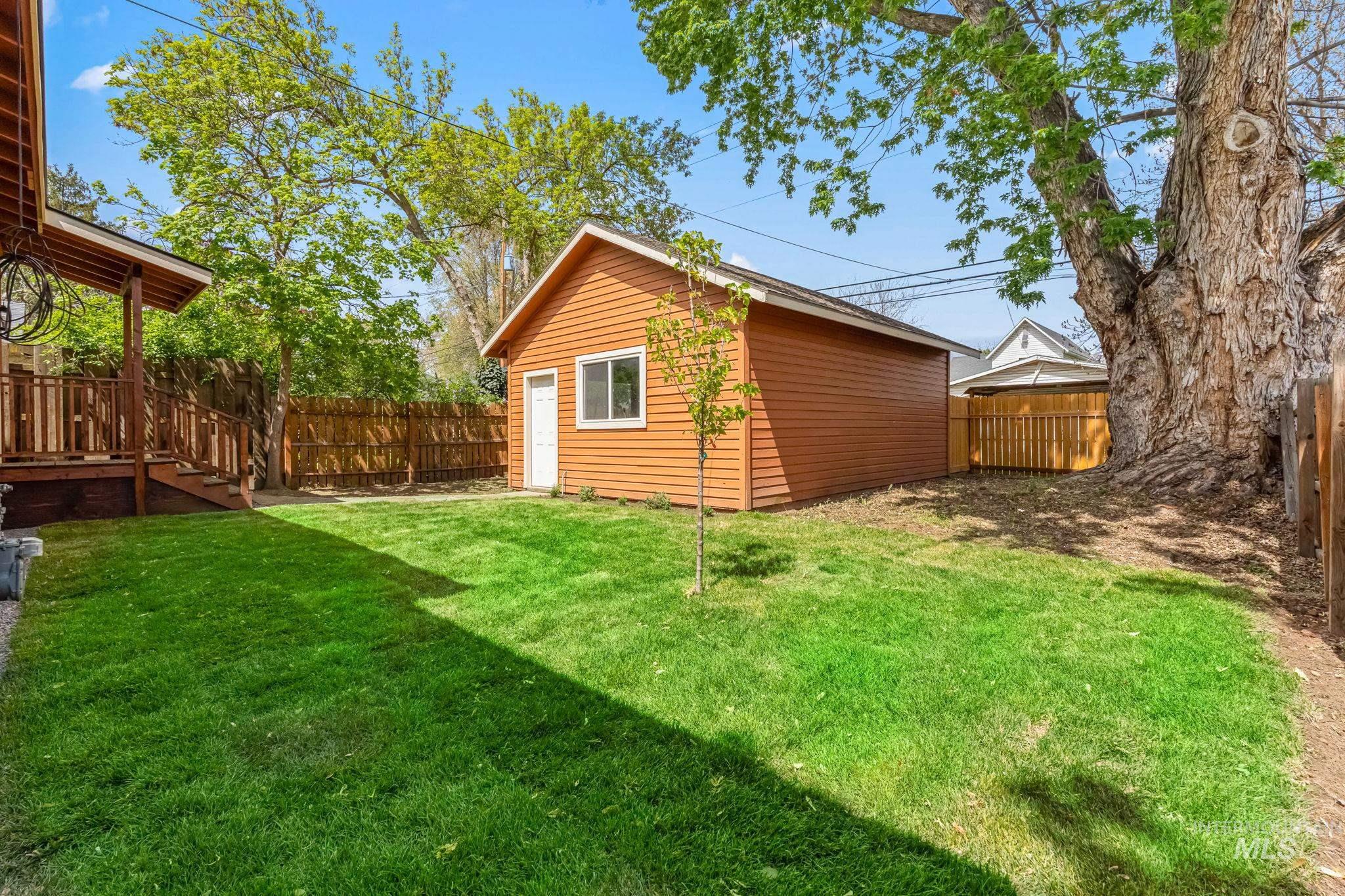 Expansive lawn featuring a detached accessory building, wood privacy fencing, and a covered porch with wood railing