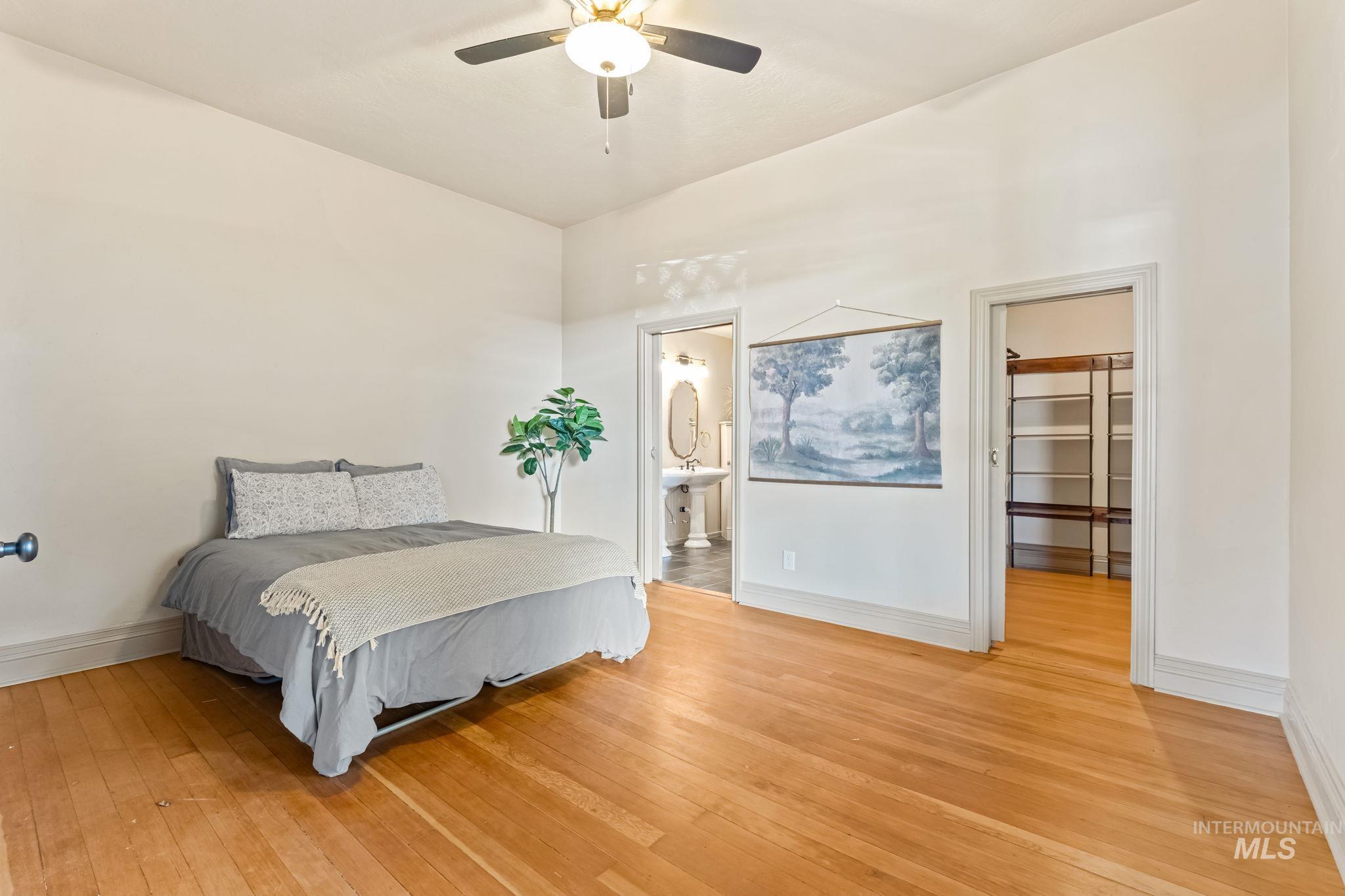 Main level primary bedroom. Spacious room featuring wood-finish flooring, a ceiling fan, and white baseboard molding