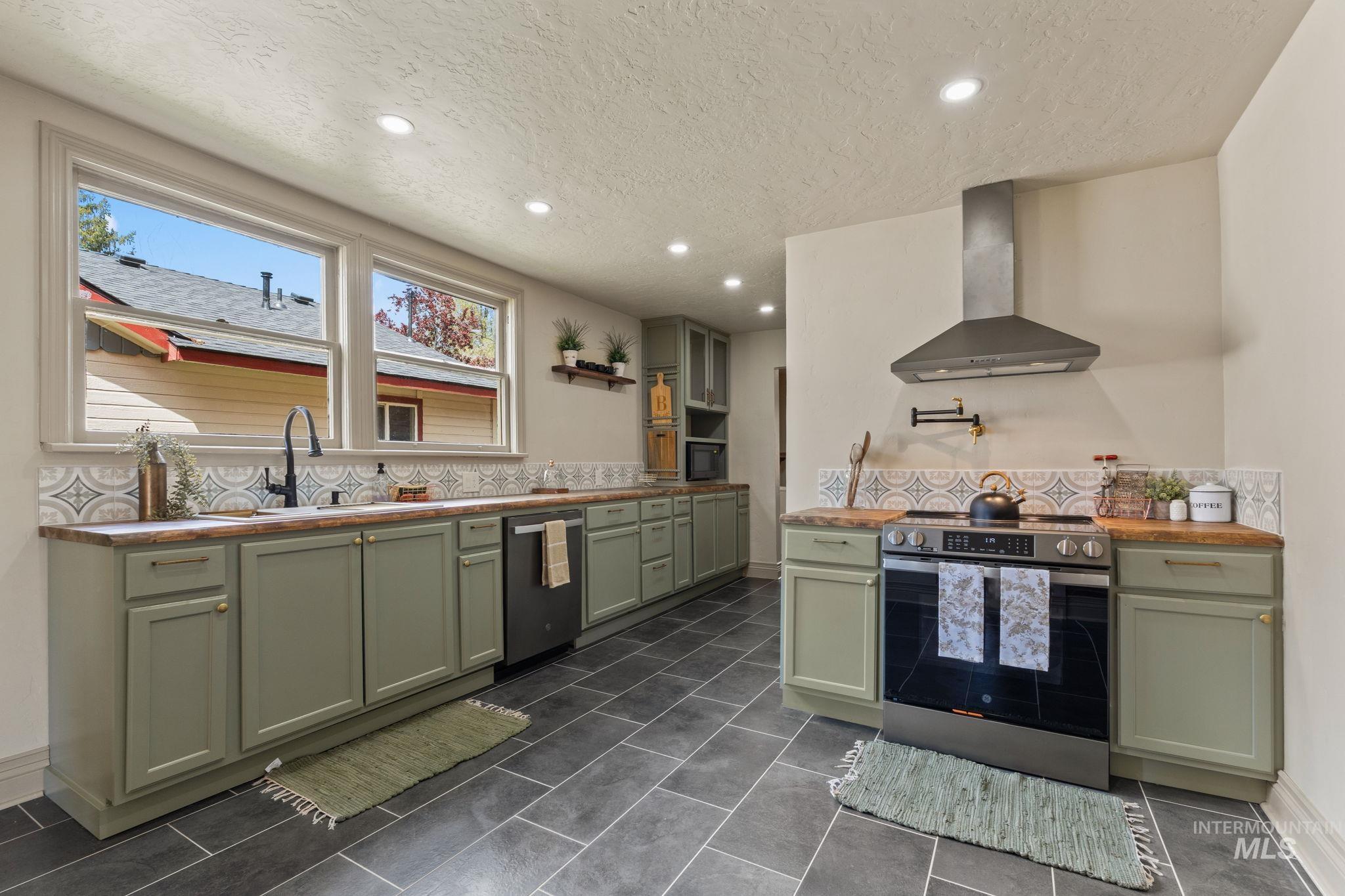 Kitchen featuring sage green cabinetry, wood-finish countertops, and dark gray tile flooring