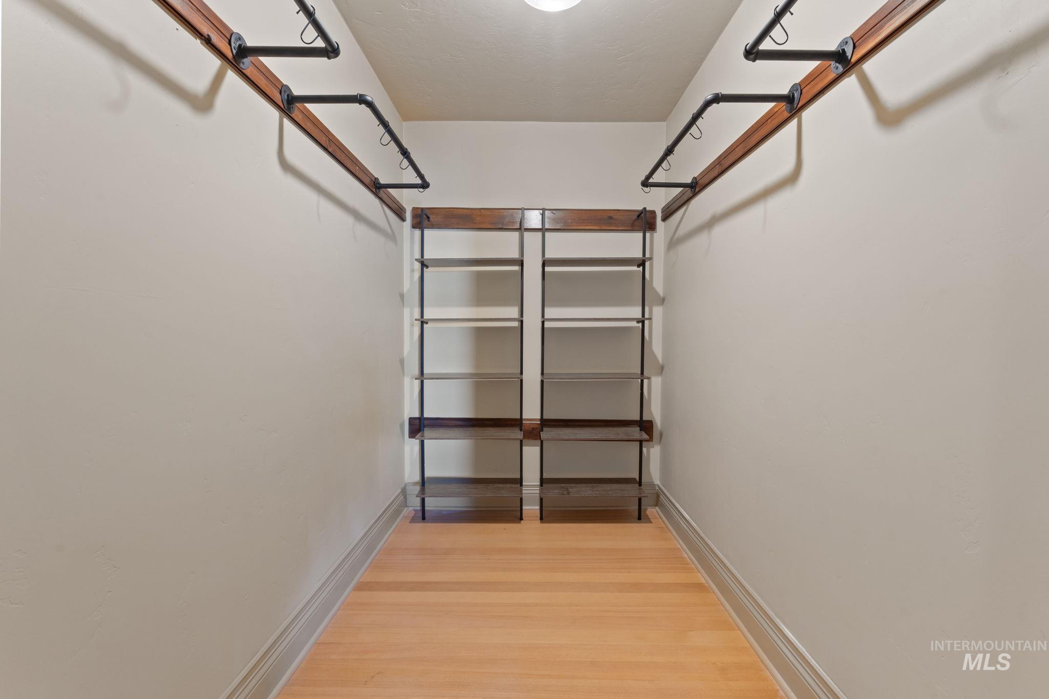 Walk-in closet featuring light wood-finish flooring, white walls, built-in shelving units, and industrial-style clothing rods