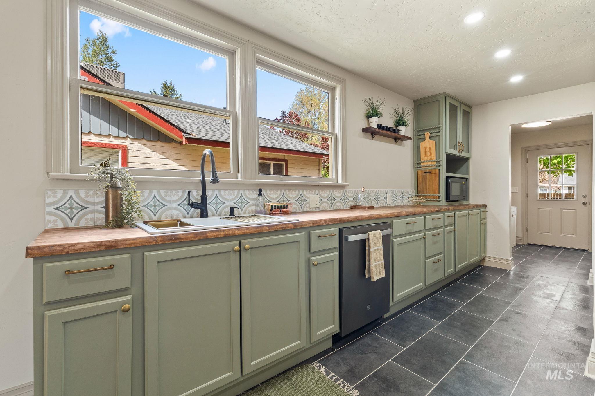 Kitchen featuring sage green cabinetry with brass hardware, wood-finish countertops, and a patterned tile backsplash