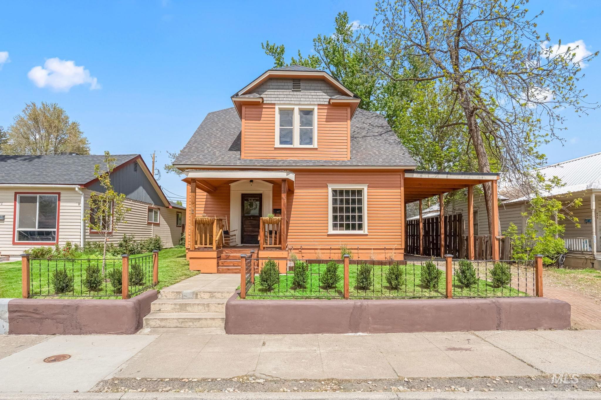 Front exterior featuring orange horizontal siding, a covered porch with natural wood railing, a gabled roofline, and a covered side entrance