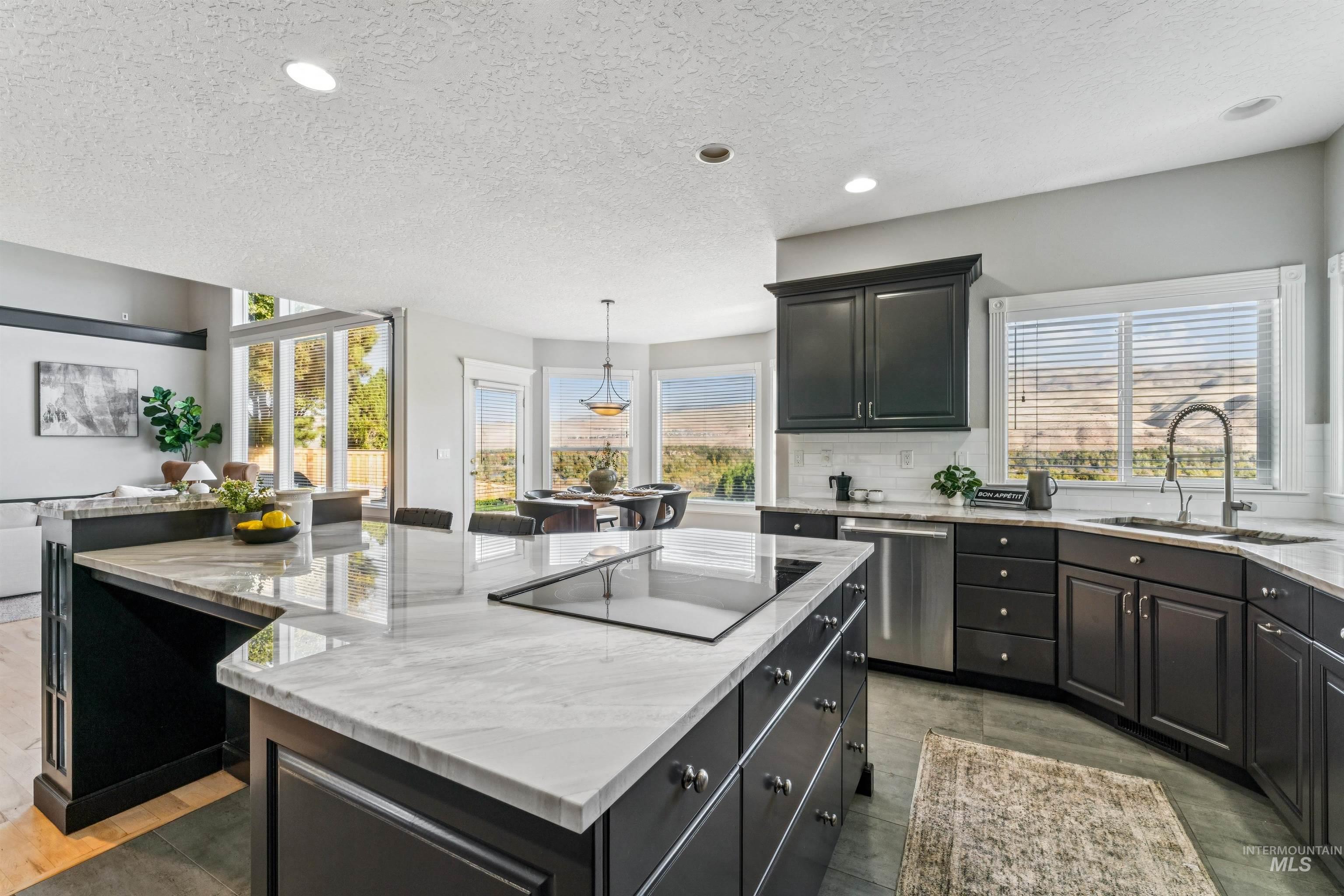 Kitchen with a spacious island, light stone counters, a textured ceiling, hanging light fixtures, and dishwasher