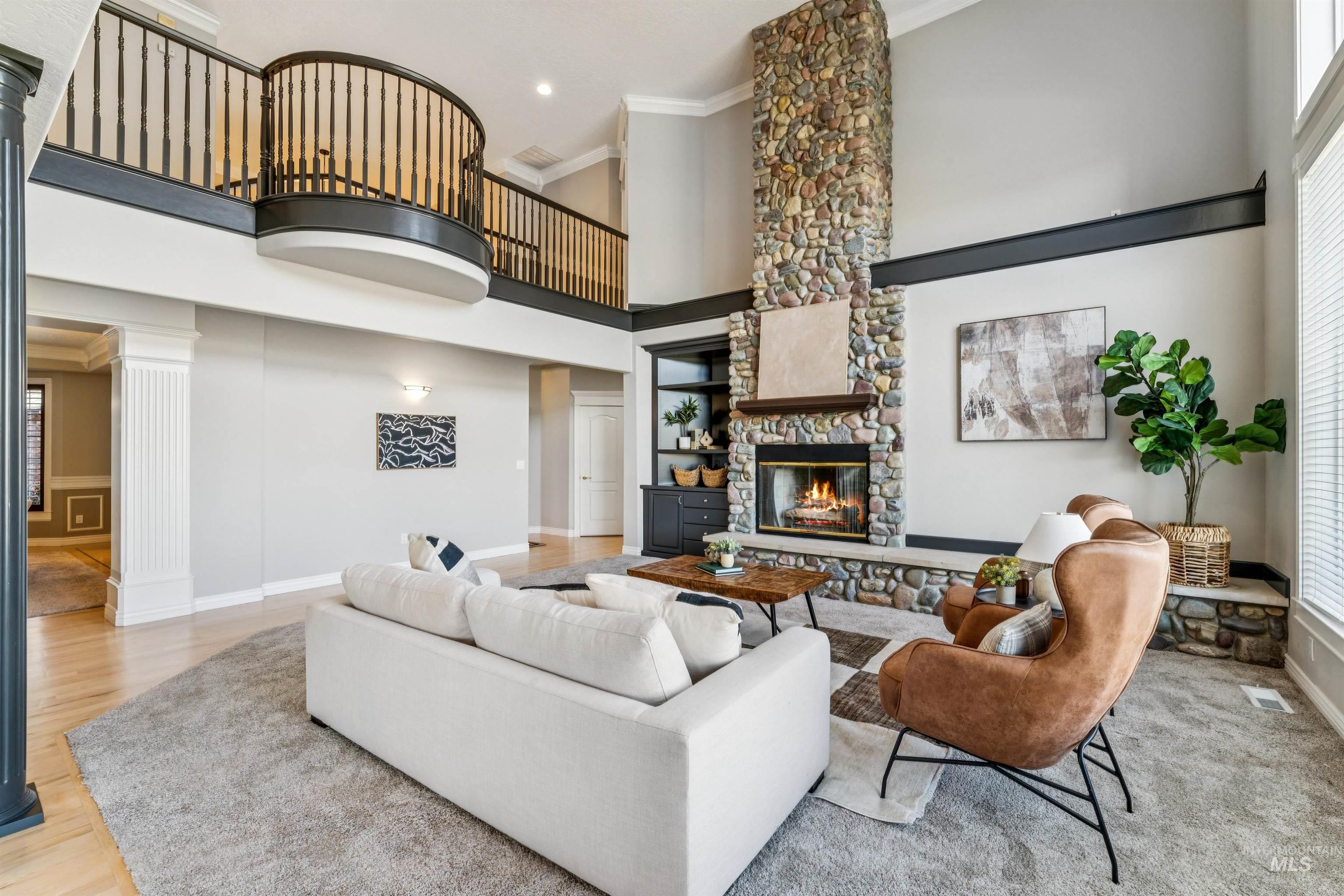 Living room with crown molding, a fireplace, a high ceiling, light wood-type flooring, and ornate columns