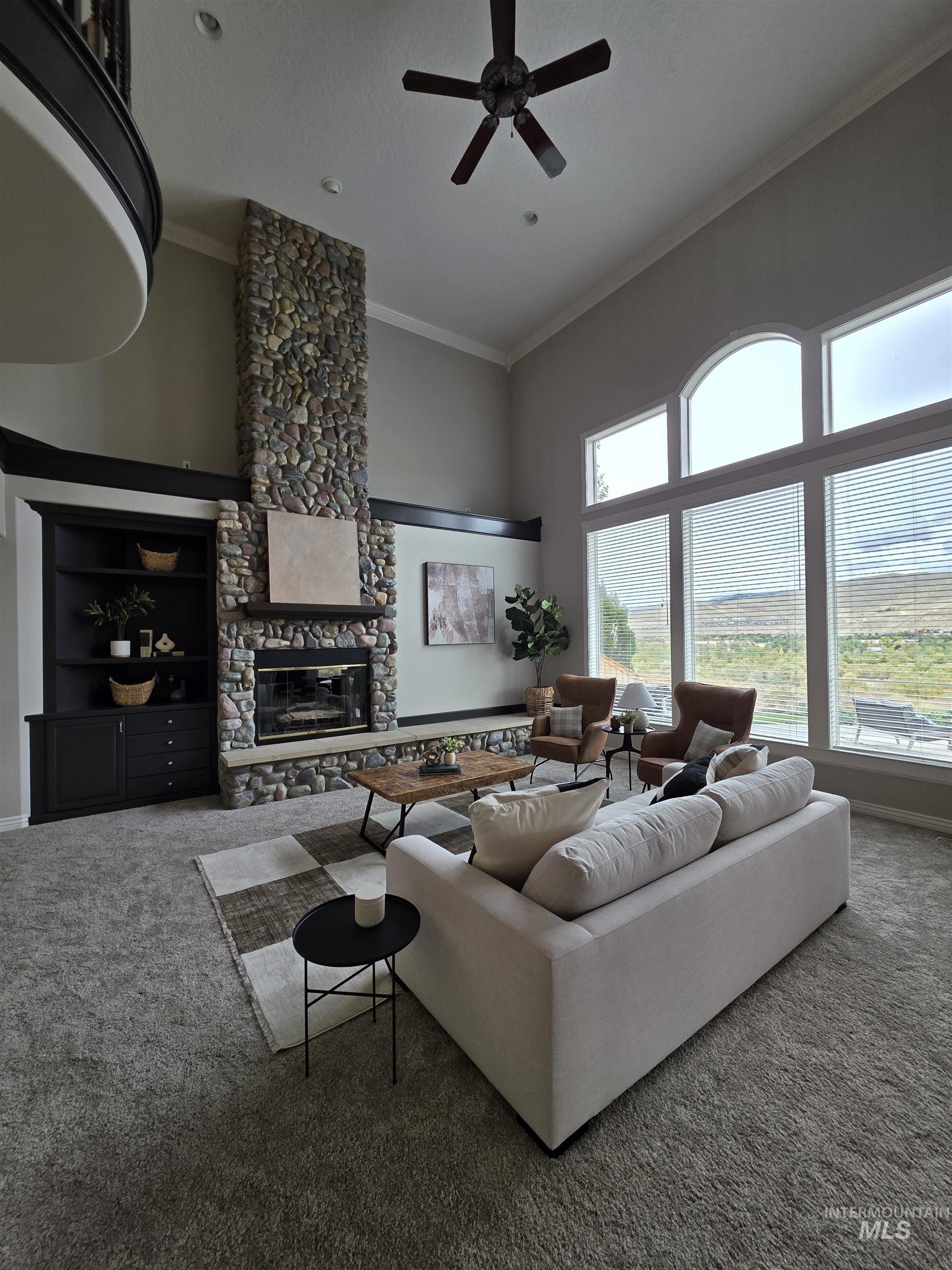 Carpeted living area with crown molding, a high ceiling, a fireplace, and a ceiling fan