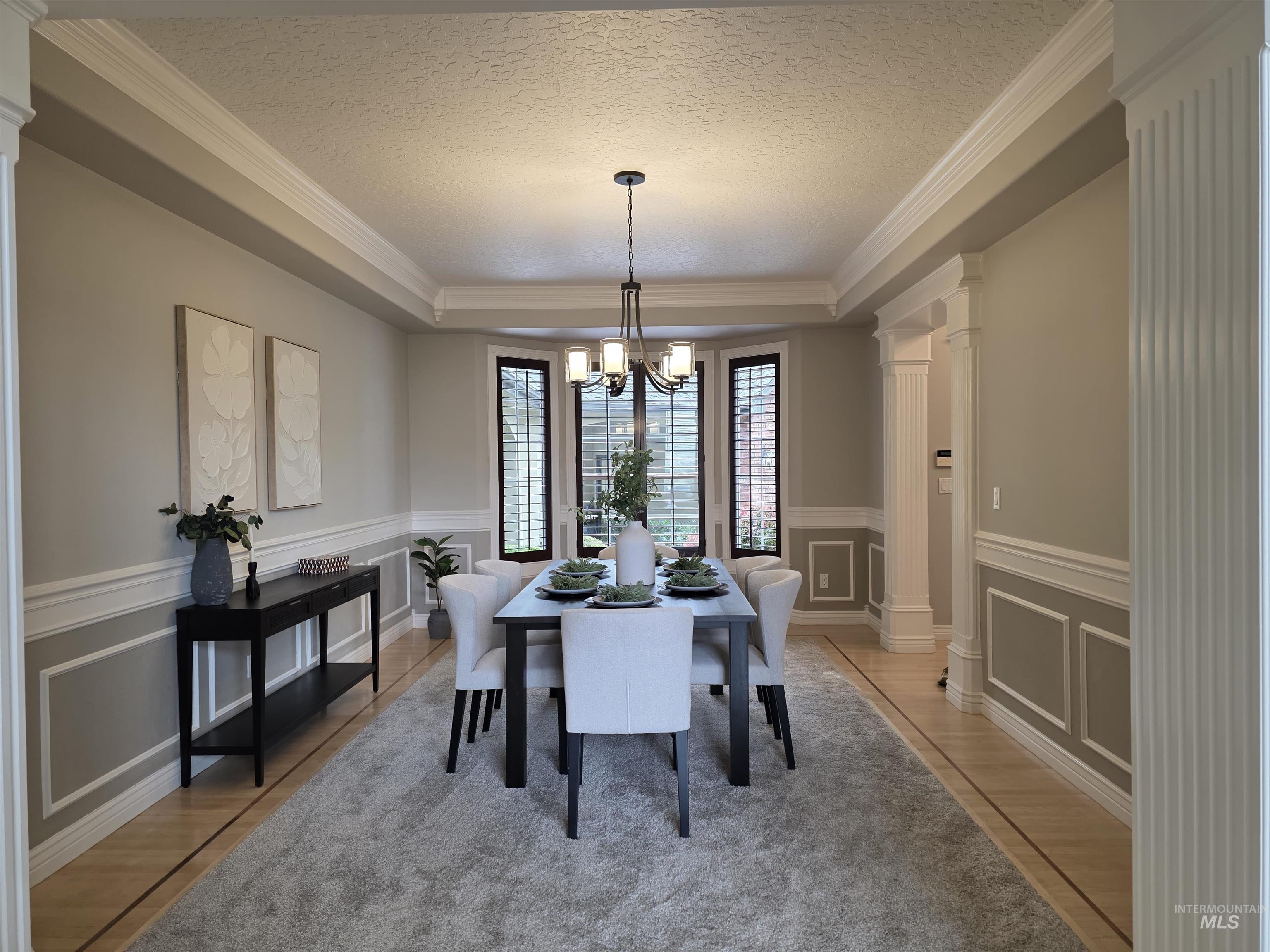 Dining room with ornate columns, a textured ceiling, a raised ceiling, crown molding, and a chandelier