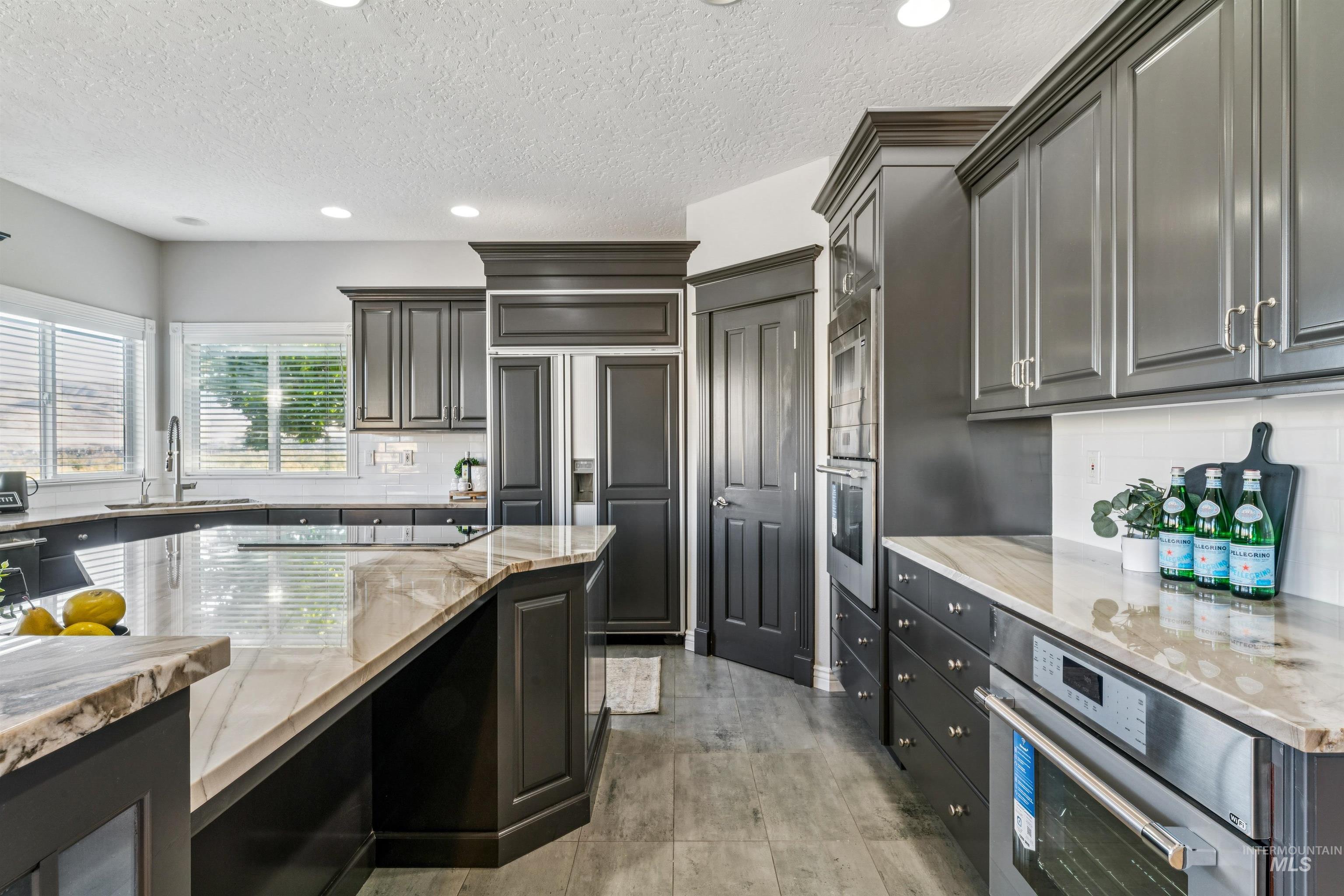 Kitchen featuring backsplash, recessed lighting, light stone countertops, paneled fridge, and a textured ceiling