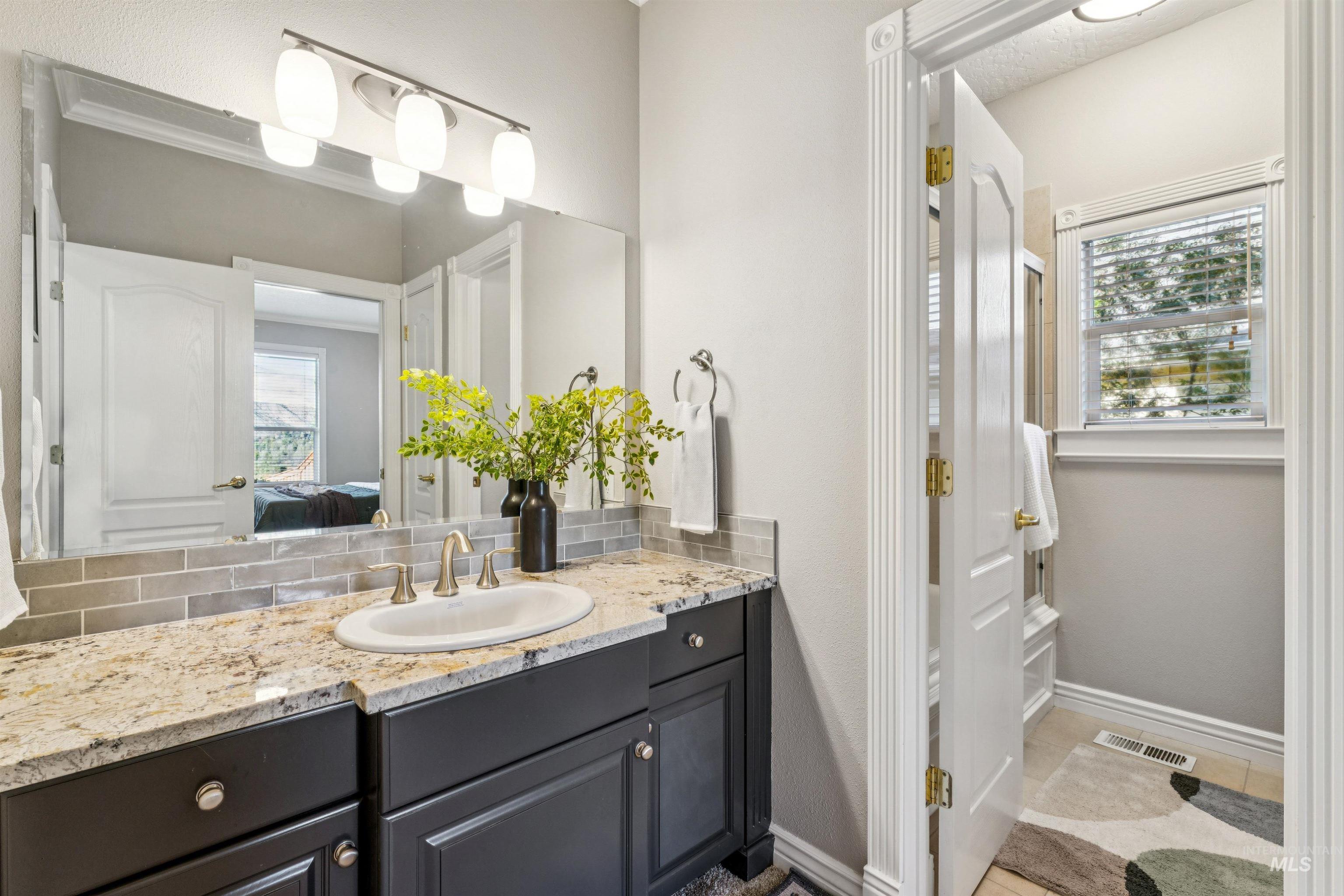 Ensuite bathroom featuring vanity, light tile patterned floors, and decorative backsplash
