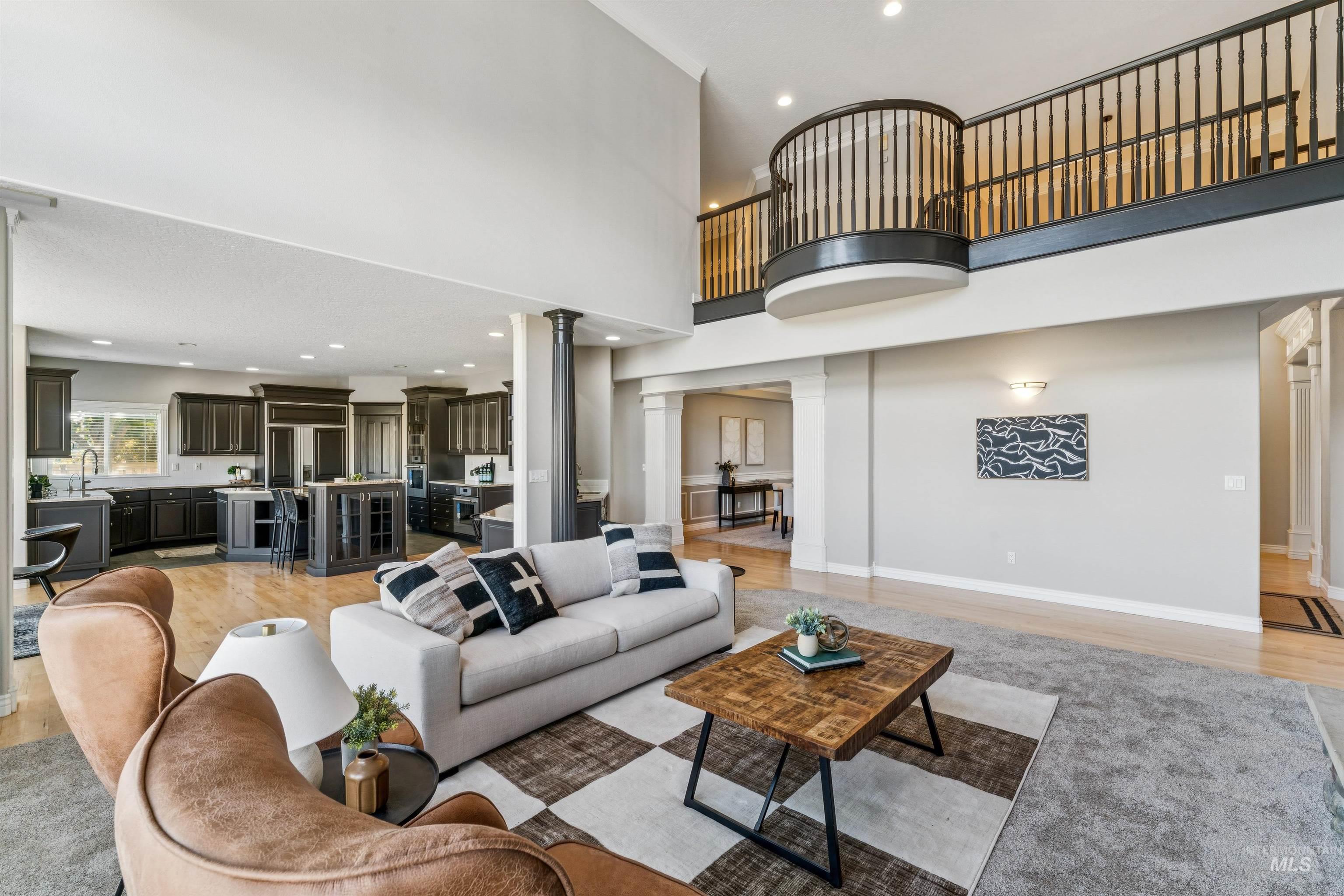 Living room with a towering ceiling, light wood-style floors, recessed lighting, and decorative columns