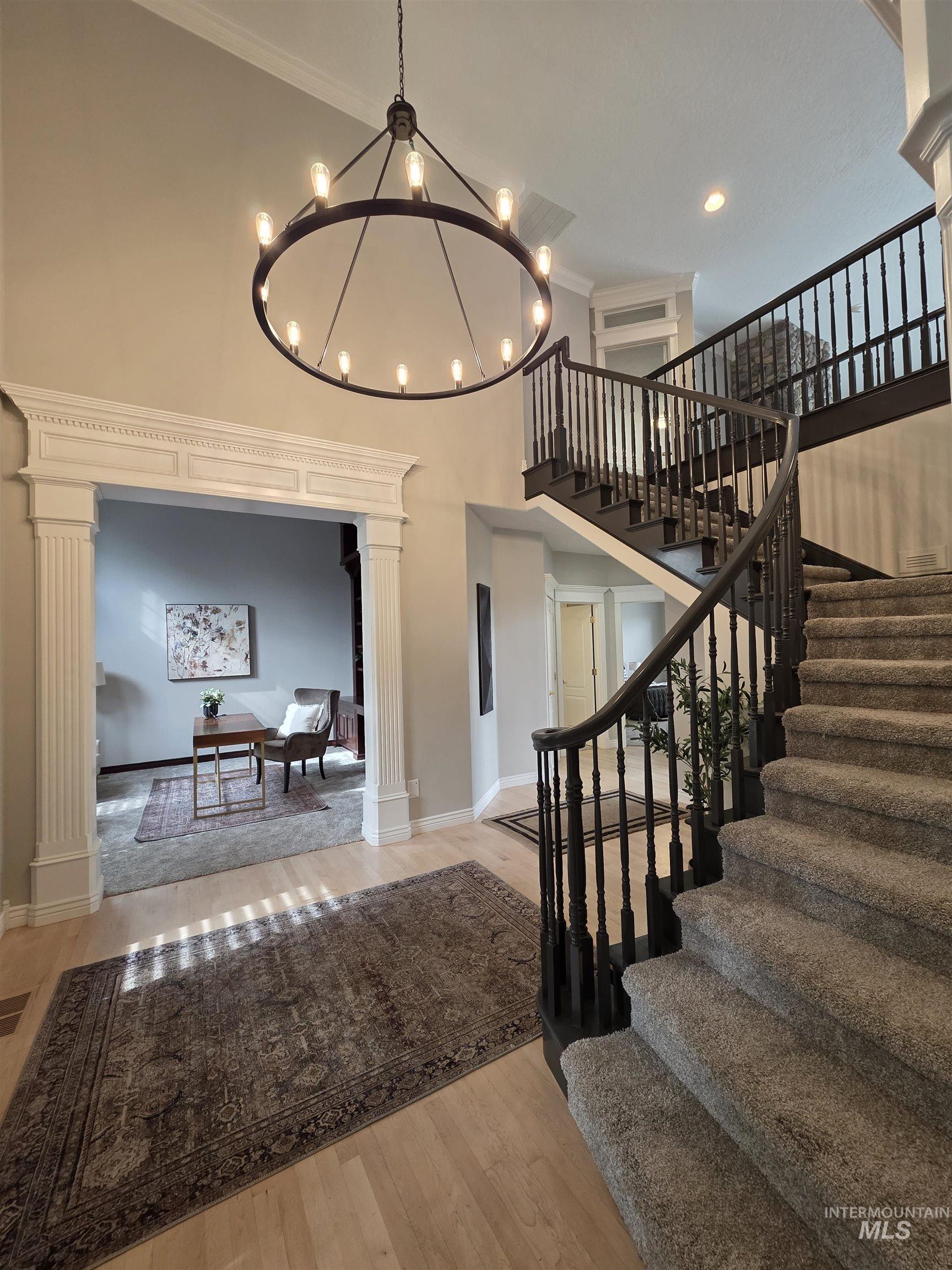 Staircase featuring ornamental molding, wood finished floors, a high ceiling, ornate columns, and a chandelier
