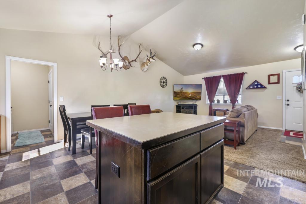 Kitchen with dark brown cabinetry, a center island, vaulted ceiling, a chandelier, and decorative light fixtures