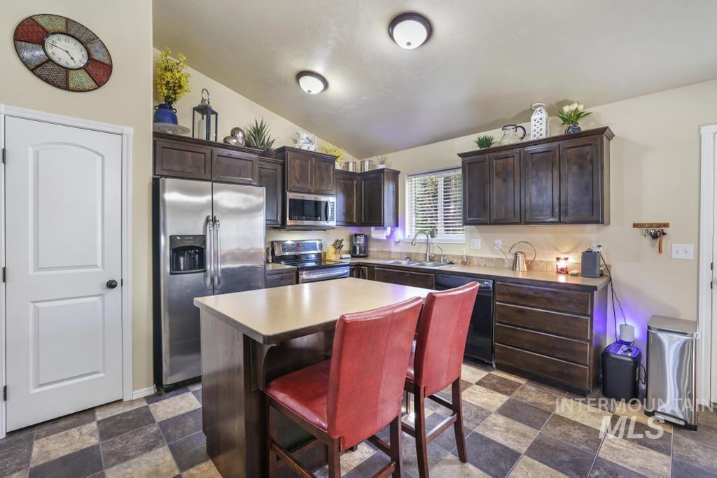 Kitchen with dark brown cabinets, a kitchen island, appliances with stainless steel finishes, lofted ceiling, and a kitchen bar