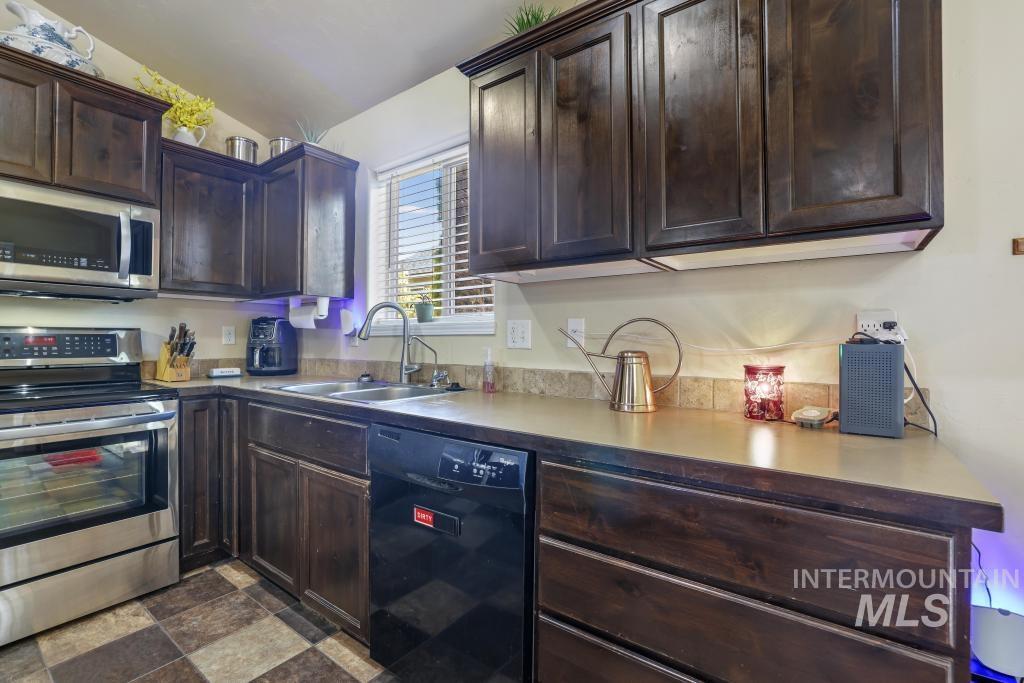 Kitchen featuring dark brown cabinetry, appliances with stainless steel finishes, stone finish floors, and light countertops