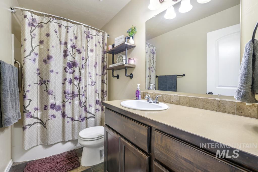 Bathroom featuring vanity, shower / bathtub combination with curtain, and dark tile patterned floors