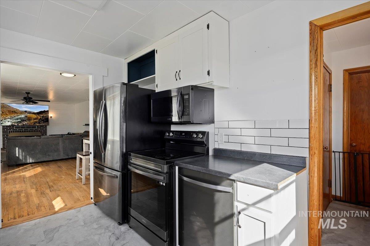 Kitchen featuring appliances with stainless steel finishes, dark countertops, white cabinetry, light wood-type flooring, and tasteful backsplash