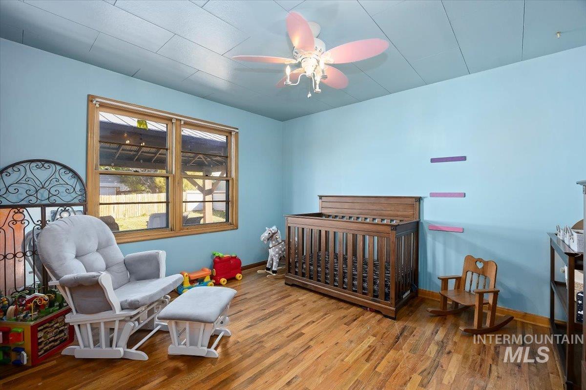 Bedroom featuring wood finished floors, a crib, and a ceiling fan