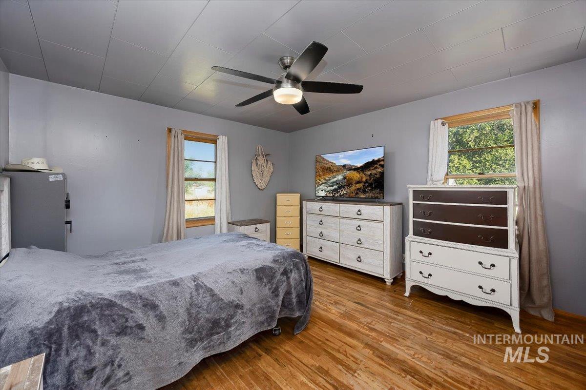 Bedroom with wood finished floors, multiple windows, and ceiling fan