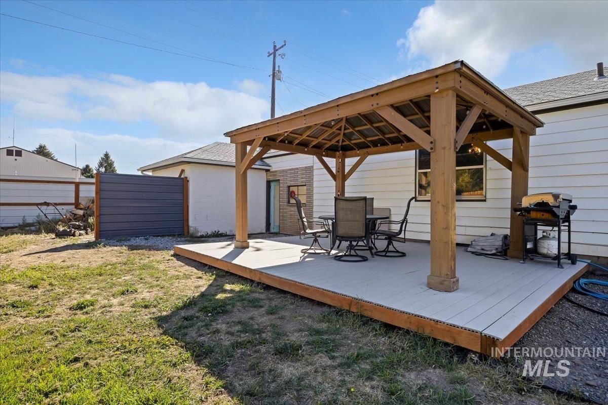 Wooden terrace featuring a gazebo, outdoor dining area, grilling area, and a yard