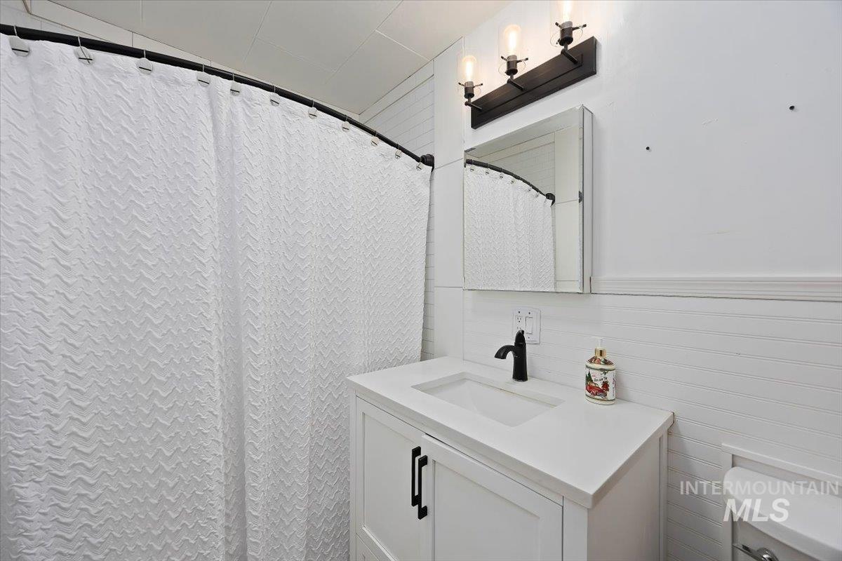Full bath featuring curtained shower, vanity, and a wainscoted wall