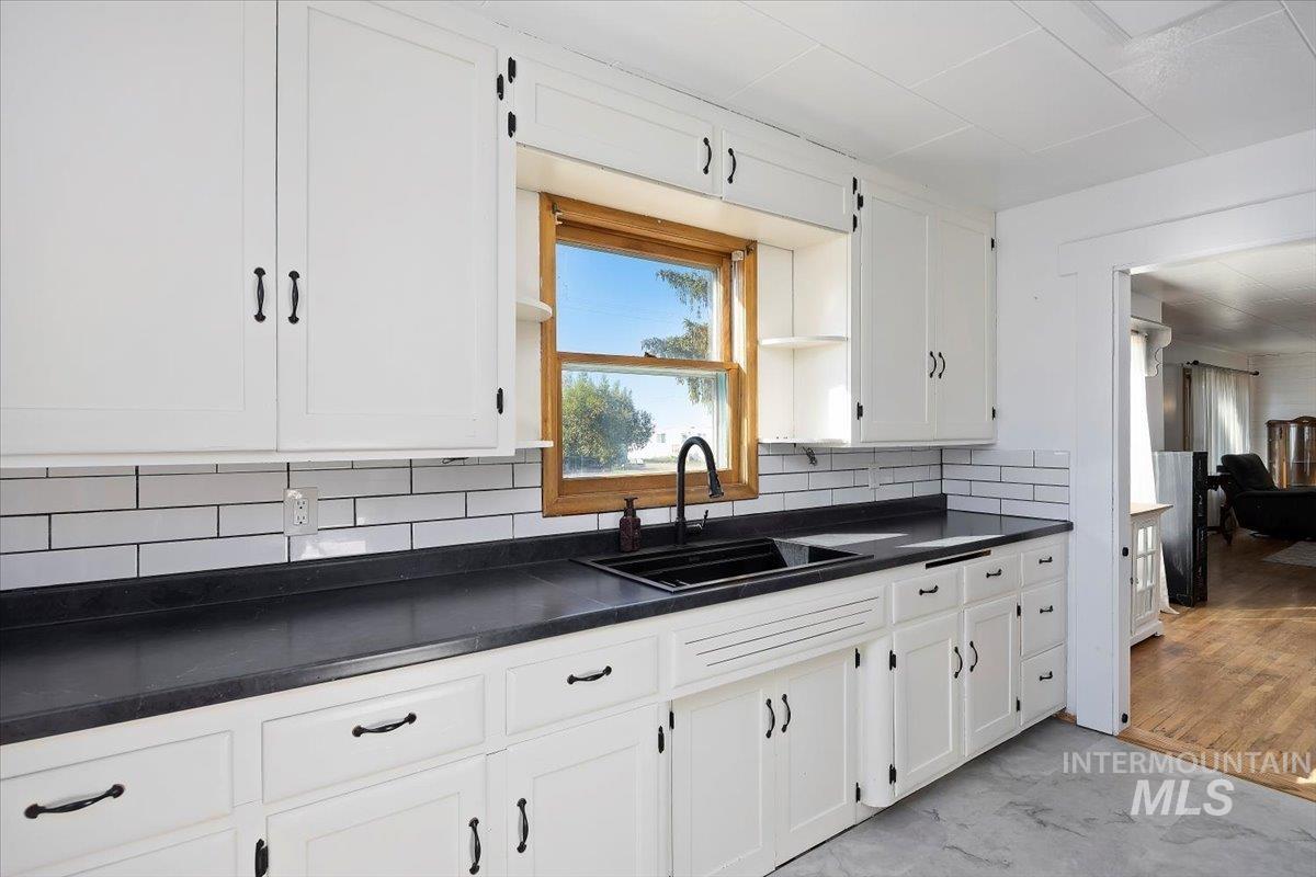 Kitchen featuring dark countertops, backsplash, and white cabinetry